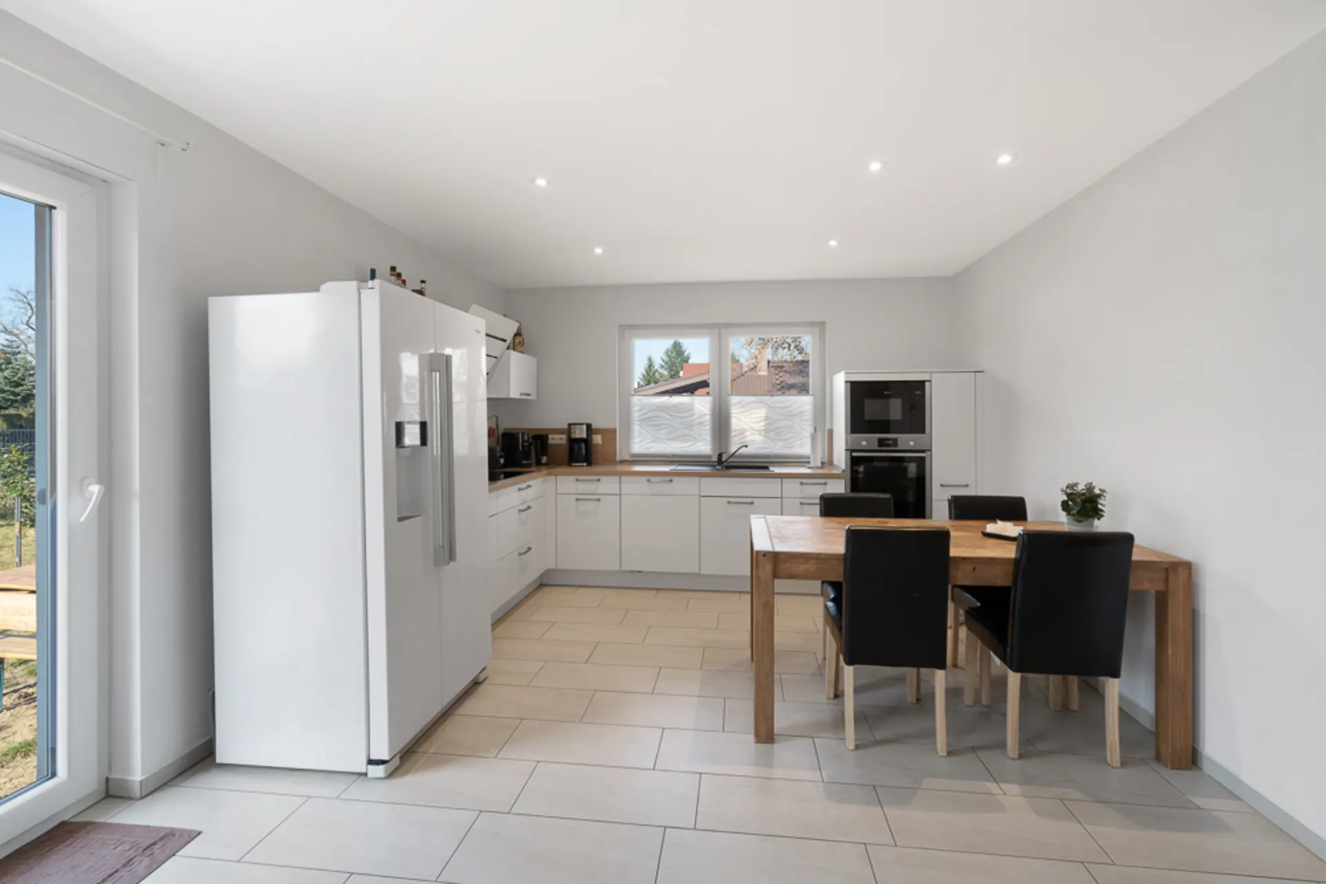 Moderne Küche mit großem Kühlschrank, Esstisch aus Holz und vier schwarzen Stühlen.