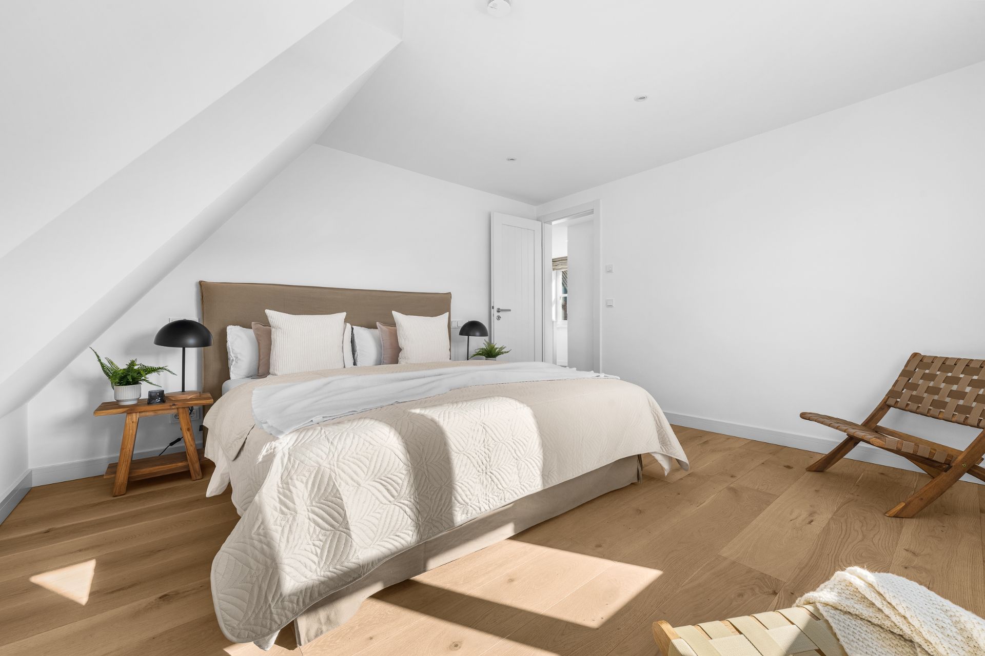 Schlafzimmer mit Doppelbett, Holzboden, Nachttischen und Stuhl unter schrägem Dach.