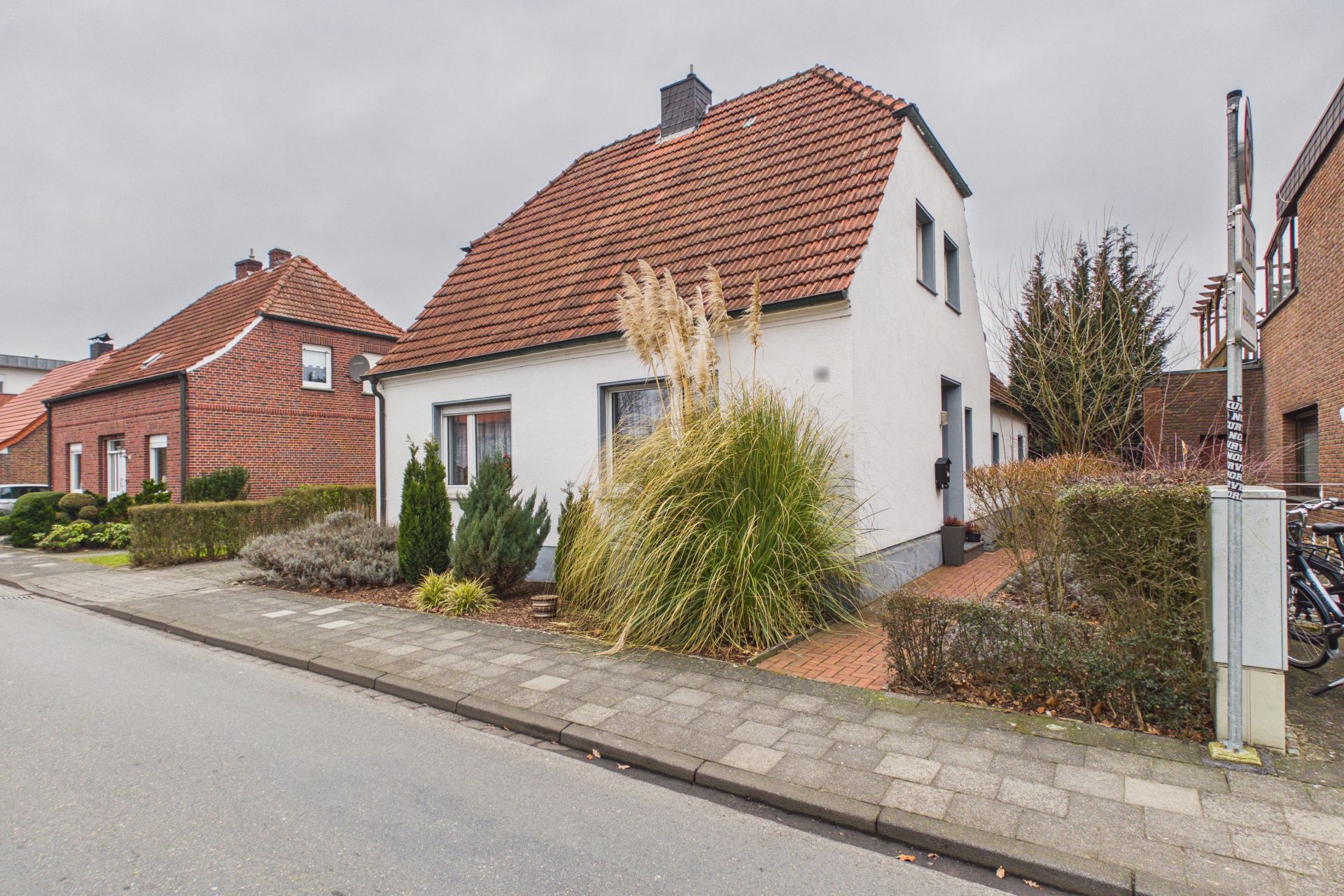 Weißes Einfamilienhaus mit rotem Dach und Vorgarten an einer Wohnstraße.