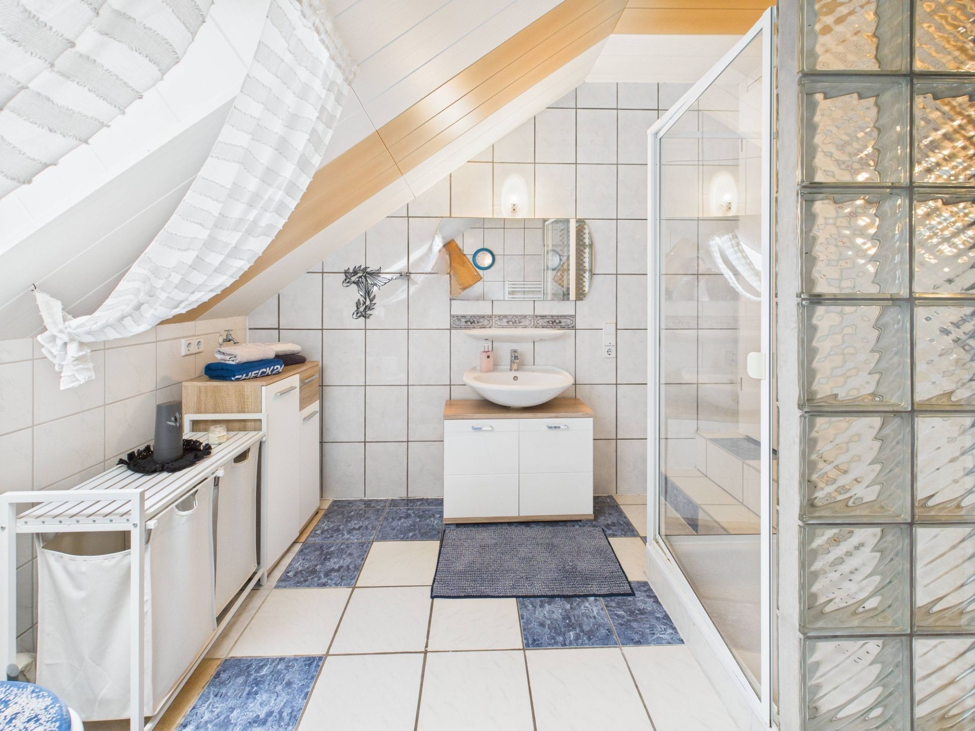 Helles Badezimmer mit Waschbecken, Spiegel, Dusche und Schräge unter dem Dach.