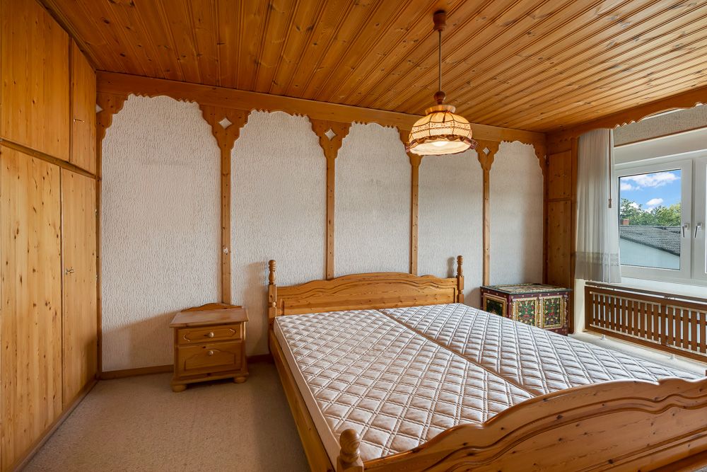 Schlafzimmer mit Holzdecke, Doppelbett, Nachttisch, Truhe, Fenster und Einbauschrank.