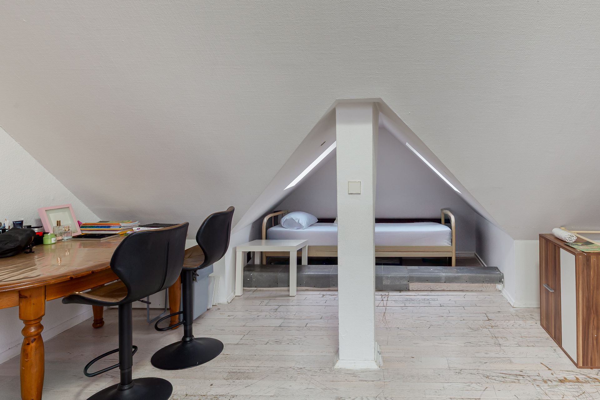 Dachzimmer mit Schreibtisch, zwei Stühlen und einem Einzelbett unter einer Dachschräge.