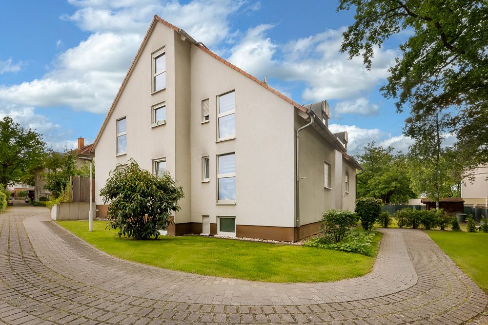 Zweistöckiges Wohnhaus mit Satteldach, umgeben von Grünfläche und gepflastertem Weg.