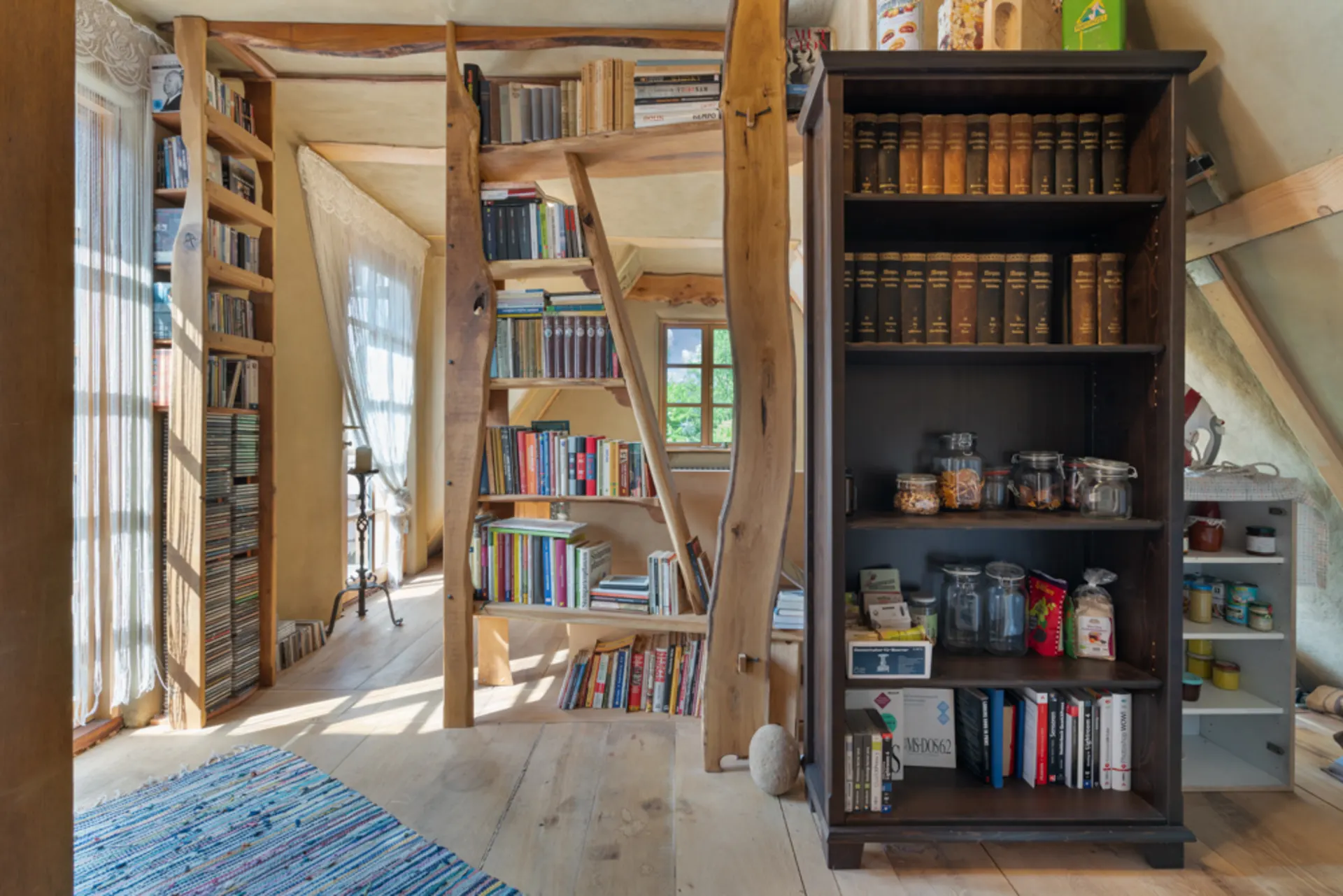 Heller Raum mit Bücherregalen, Gläsern, Vorräten und schrägen Holzbalken.