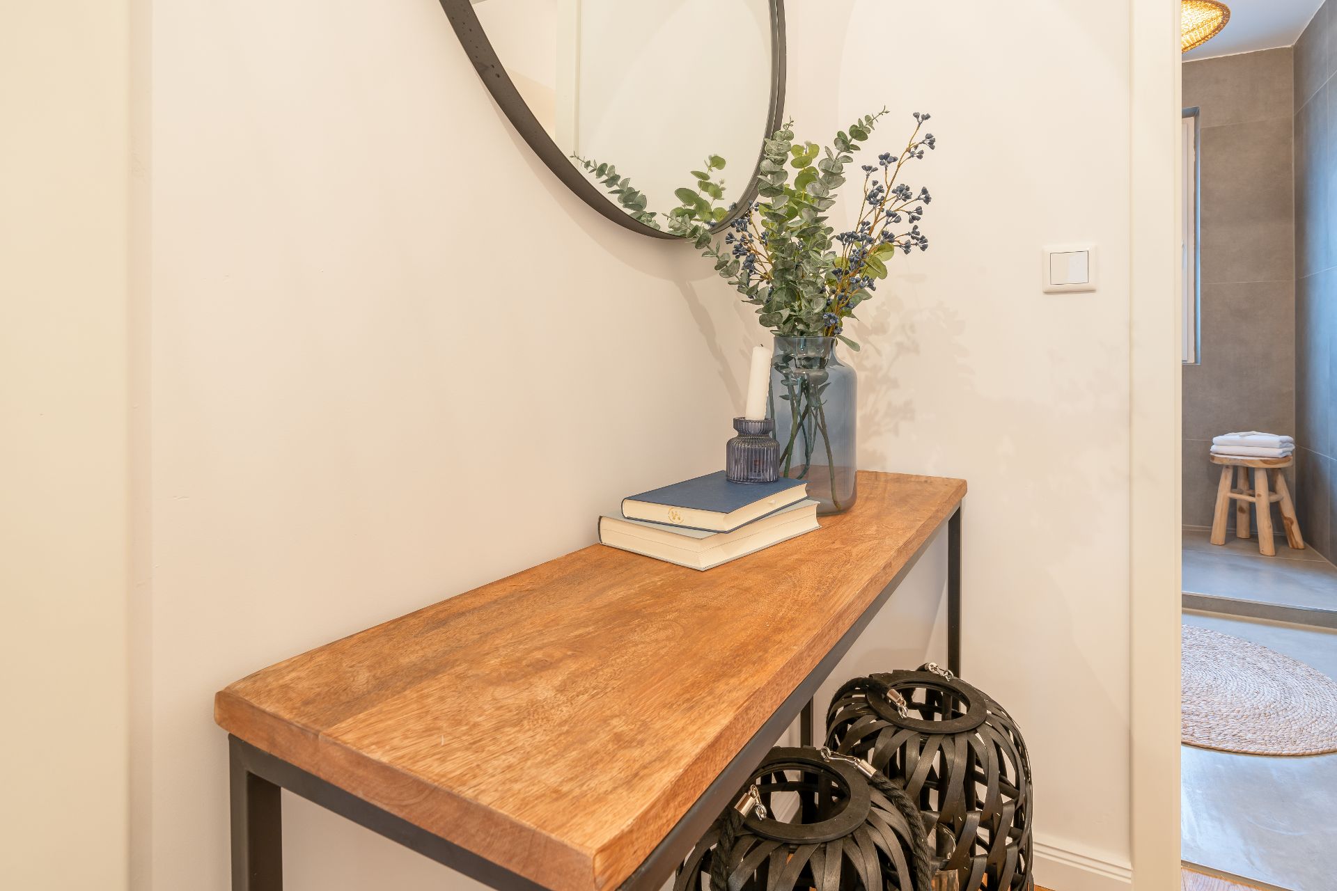 Holztisch im Flur mit Vase, Büchern, Kerze und rundem Spiegel an der Wand.