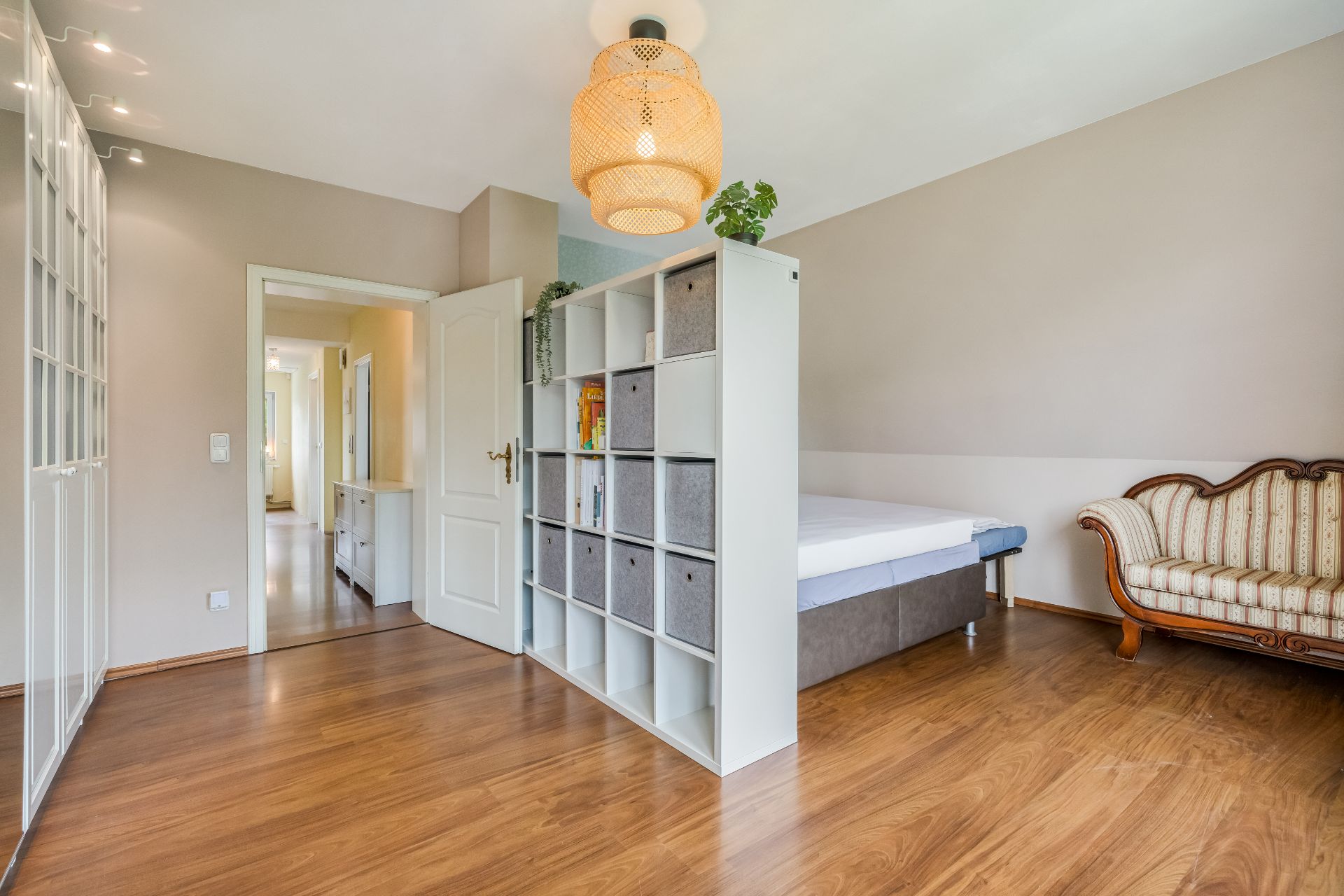 Helles Zimmer mit Holzfußboden, Regal als Raumteiler, Bett und vintage Sofa.