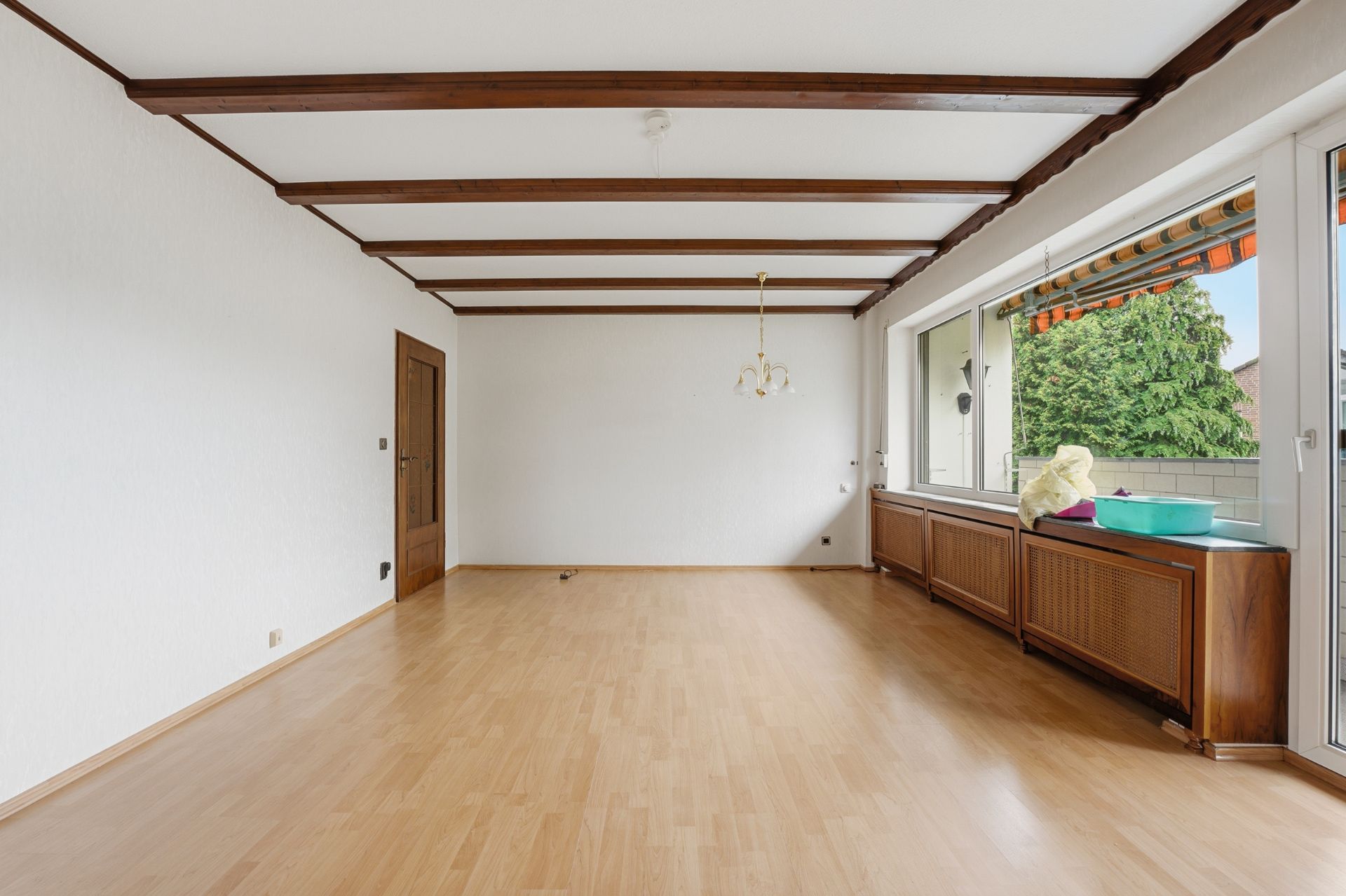 Helles Wohnzimmer mit Holzboden, Deckenbalken und großen Fenstern zur Terrasse.