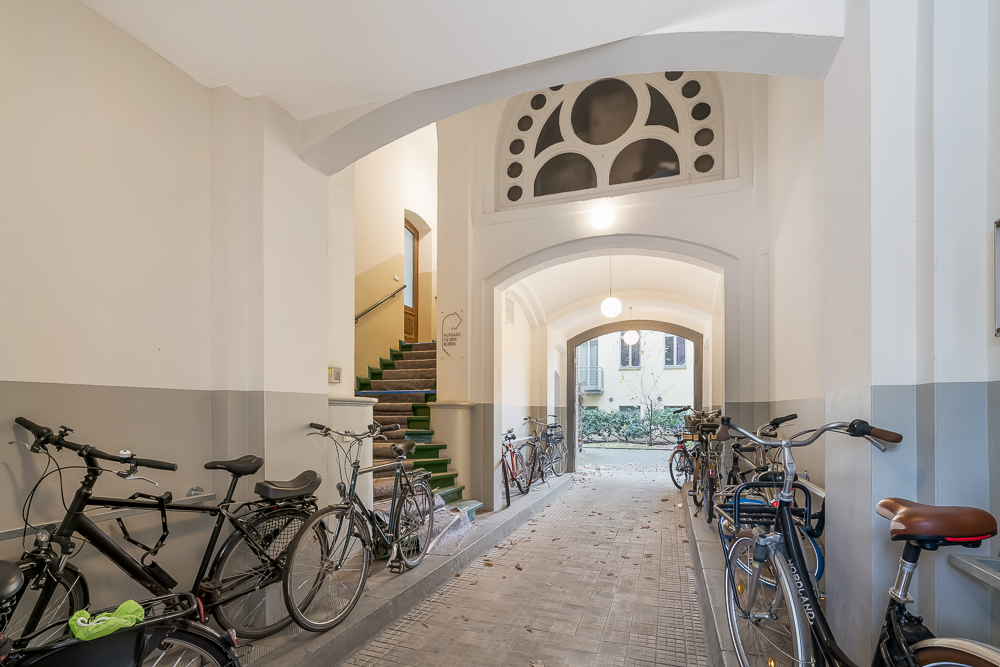 Helle Durchfahrt mit mehreren abgestellten Fahrrädern und grüner Treppe im Hintergrund.