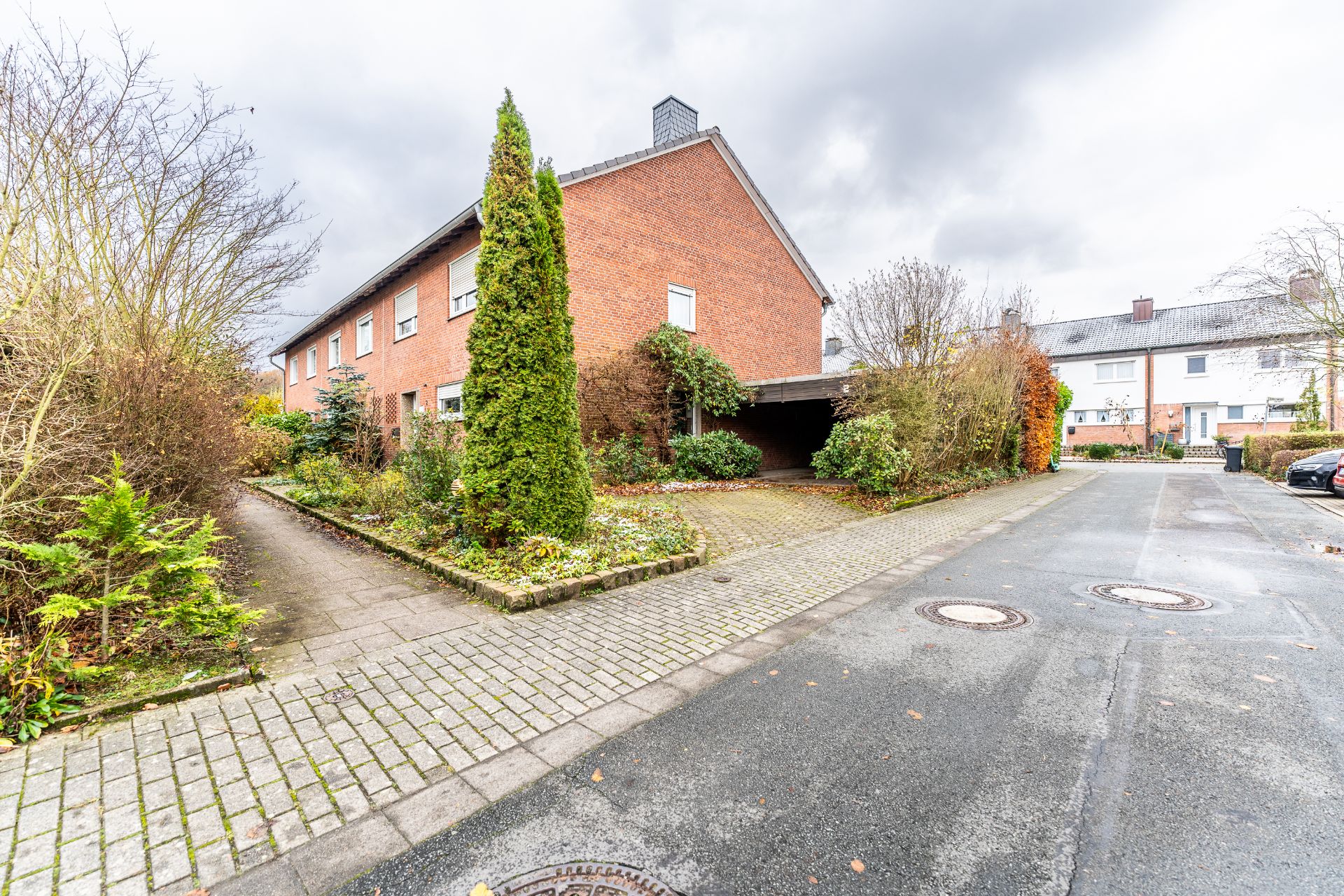Backstein-Reihenhaus mit Vorgarten und Carport an einer ruhigen Wohnstraße.