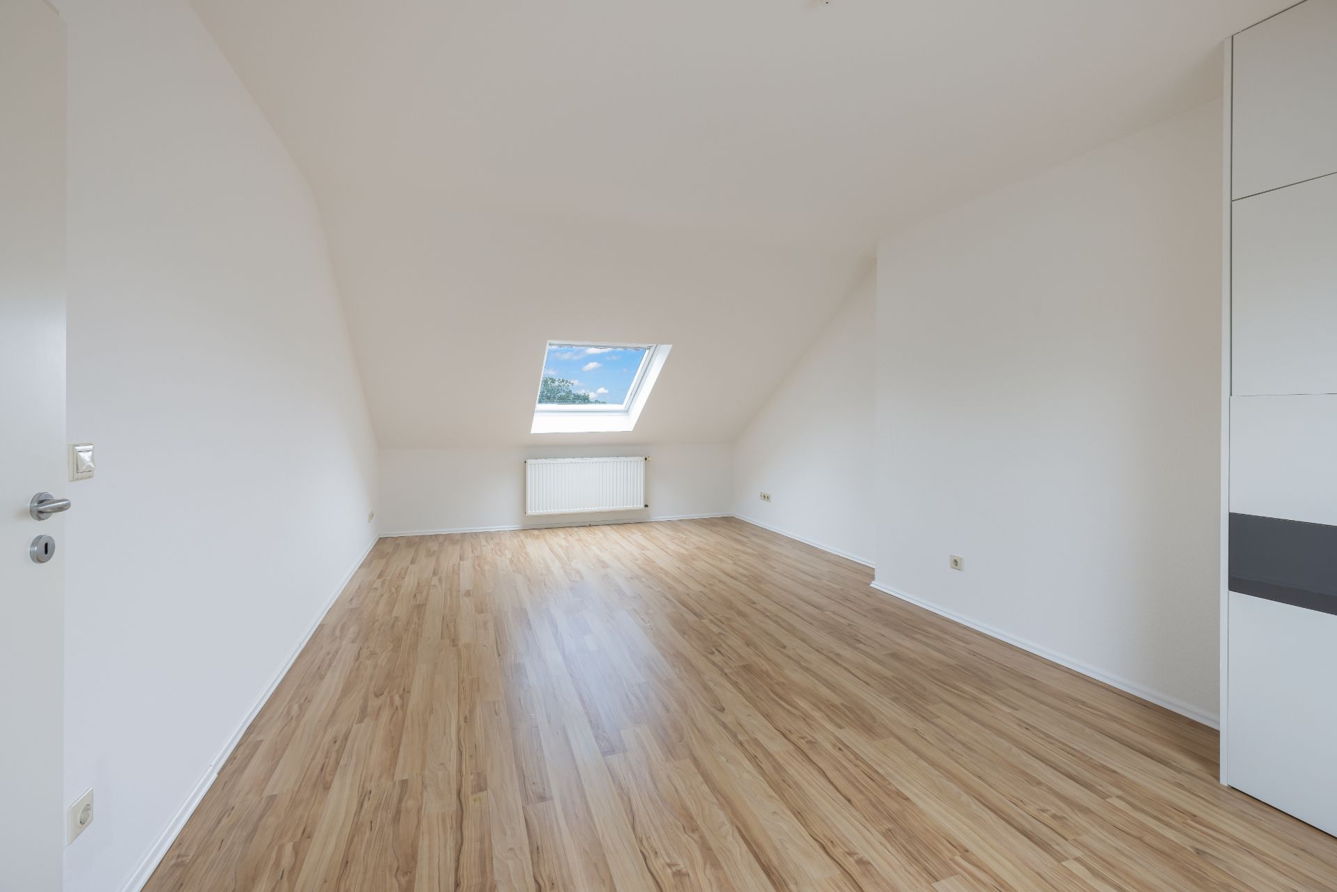 Leerer Raum mit Holzfußboden, Dachschrägen und großem Dachfenster.