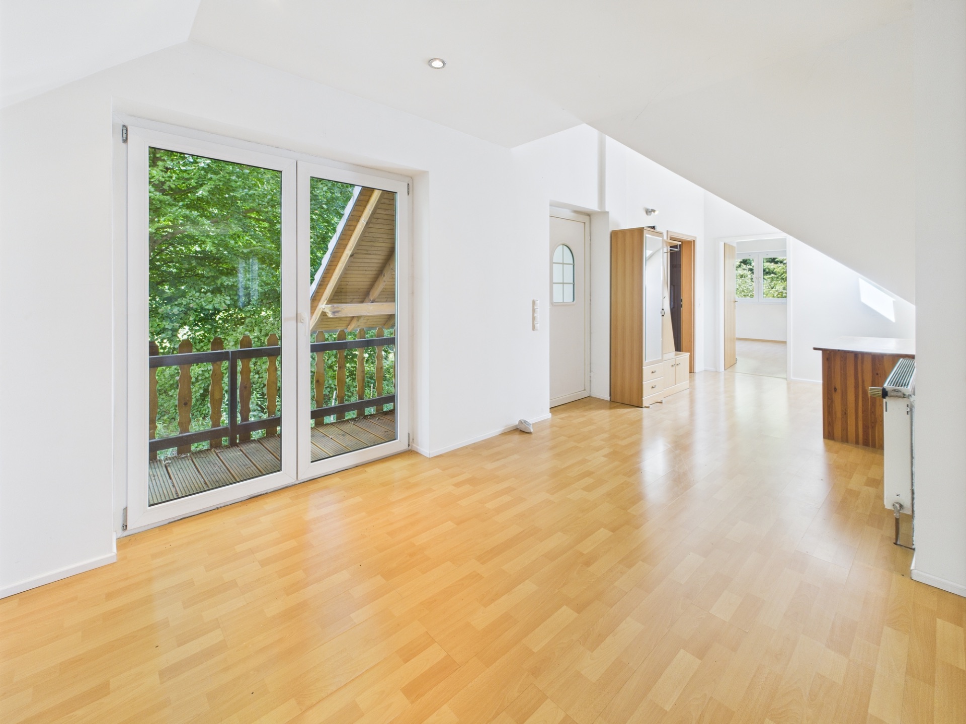 Heller Raum mit Parkettboden, großen Fenstern und Zugang zu einem Balkon mit Holzgeländer.