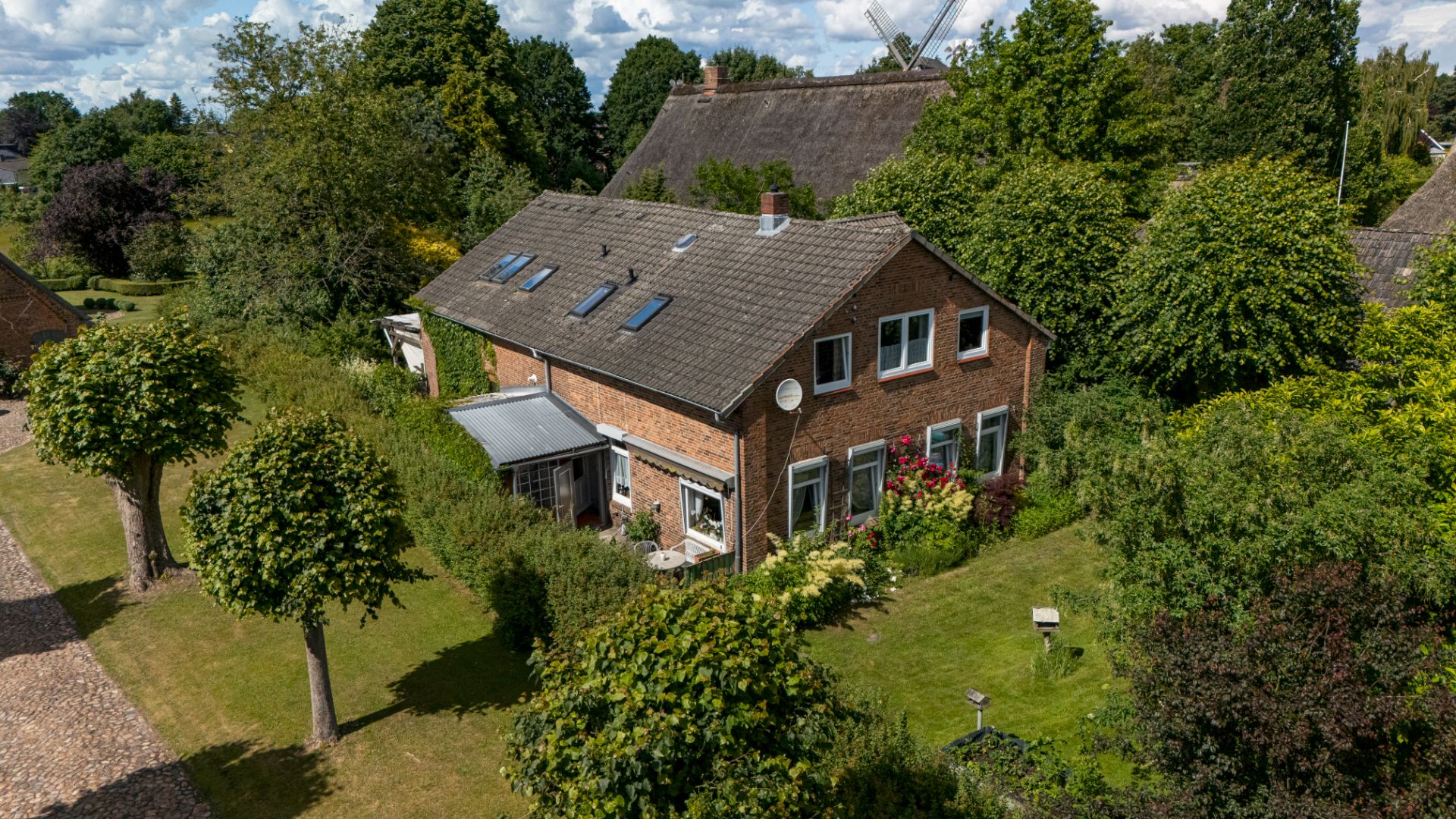 Backsteinhaus mit Satteldach, Garten und Bäumen, aufgenommen aus der Vogelperspektive.
