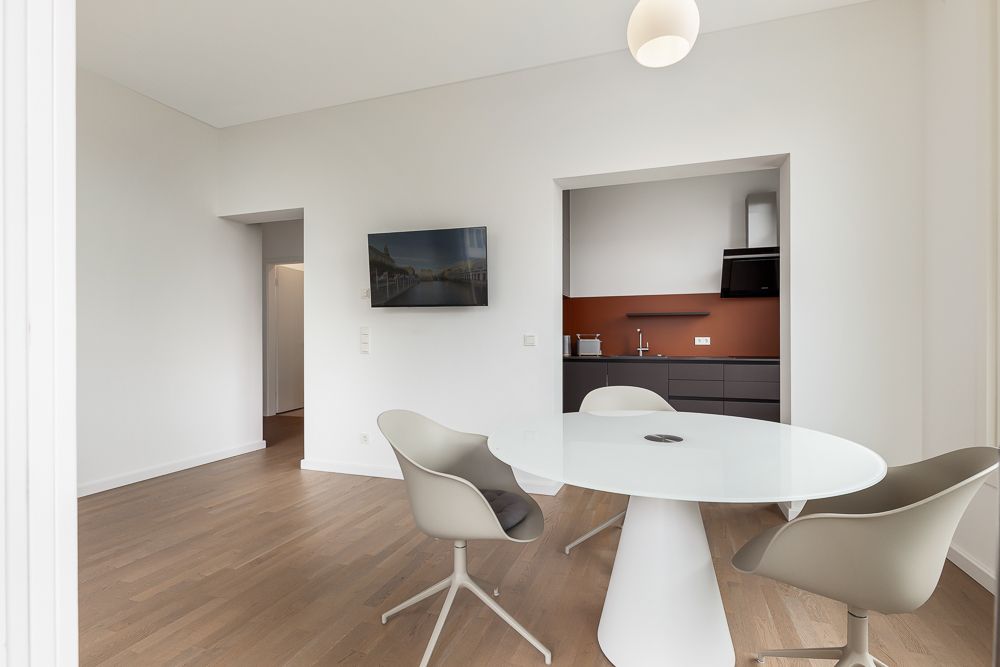 Essbereich mit rundem Tisch, drei Stühlen und Blick in eine kleine moderne Küche.