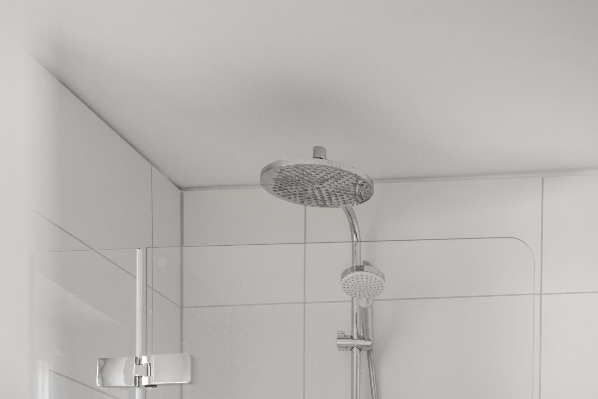 Moderne Dusche mit runder Regenbrause und Handbrause vor weißen Fliesen.