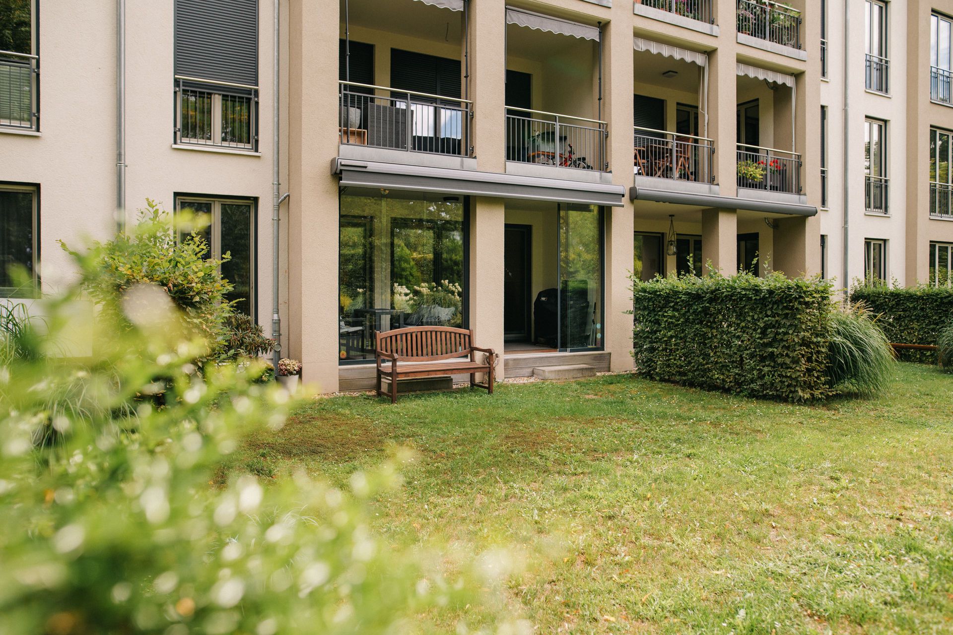 Wohnhaus mit Balkonen und einer Holzbank im Garten vor dem Gebäude.
