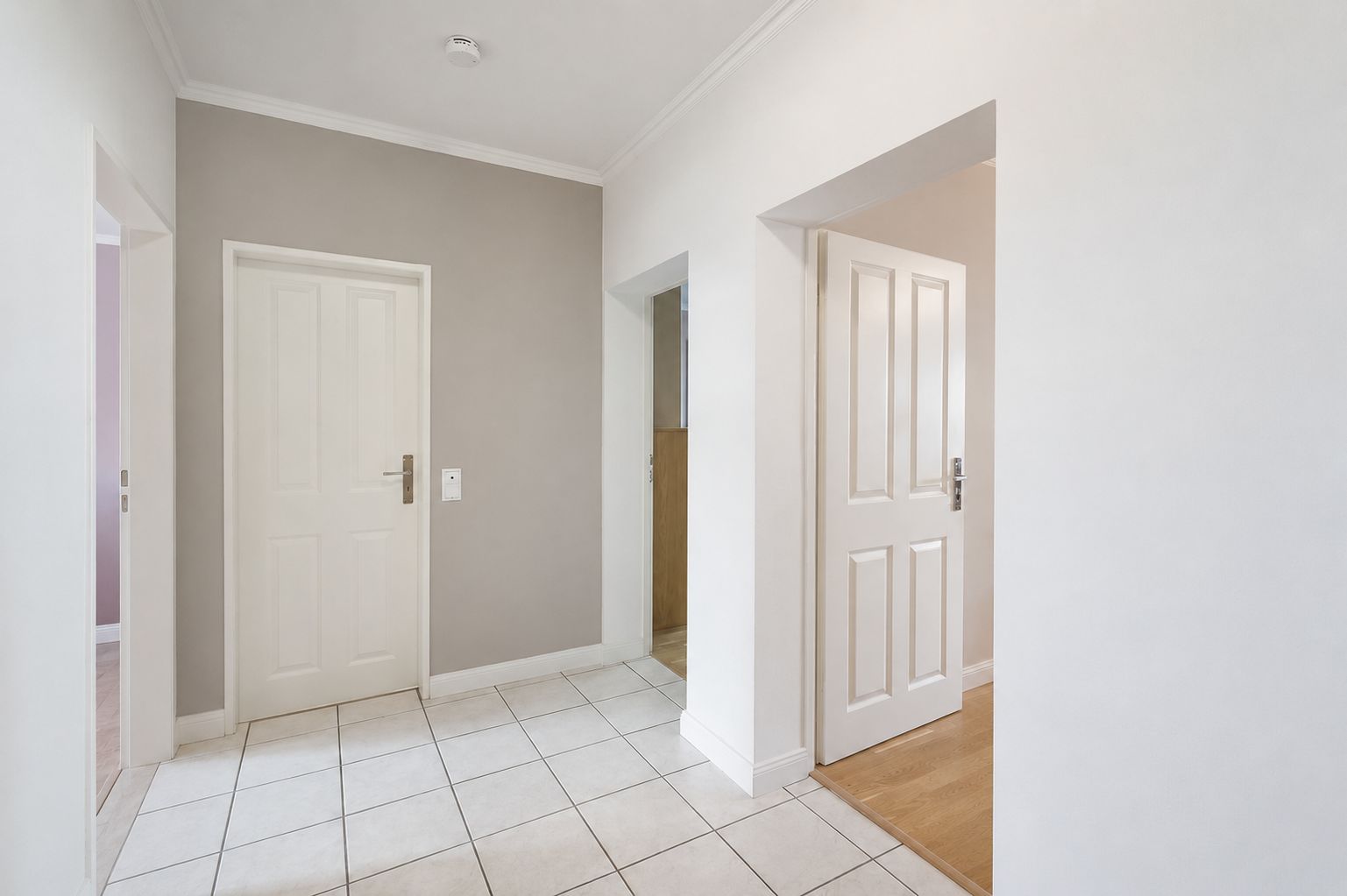 Heller Flur mit weißen Türen, Fliesenboden und beigen Wänden in einer Wohnung.