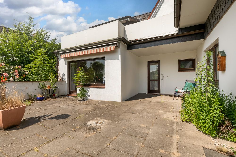 Terrasse mit Steinboden, Pflanzen, Markise und Glas-Schiebetür an einem Wohnhaus.