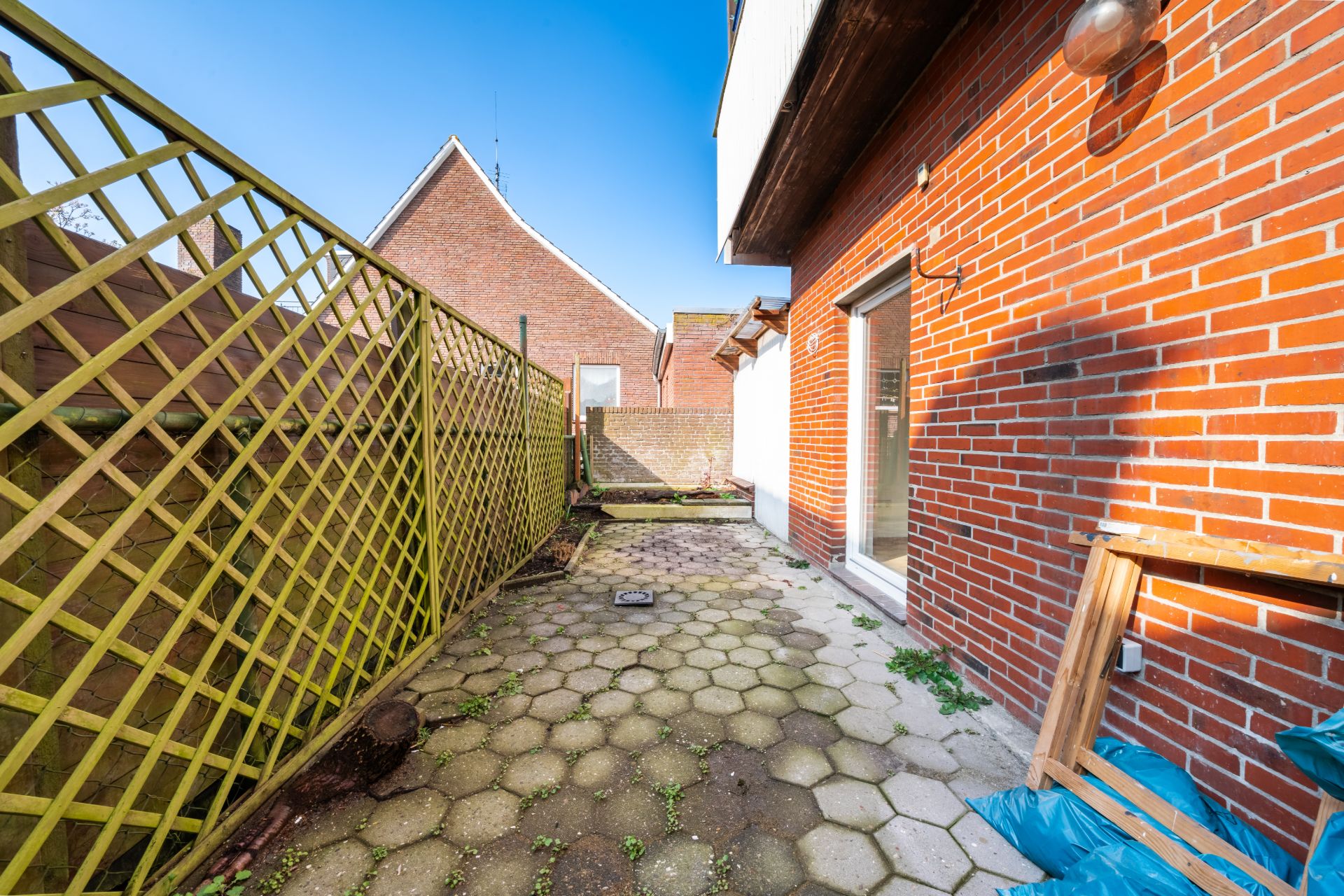Kleiner Hinterhof mit Steinboden, Holzzaun und roter Backsteinwand eines Hauses.