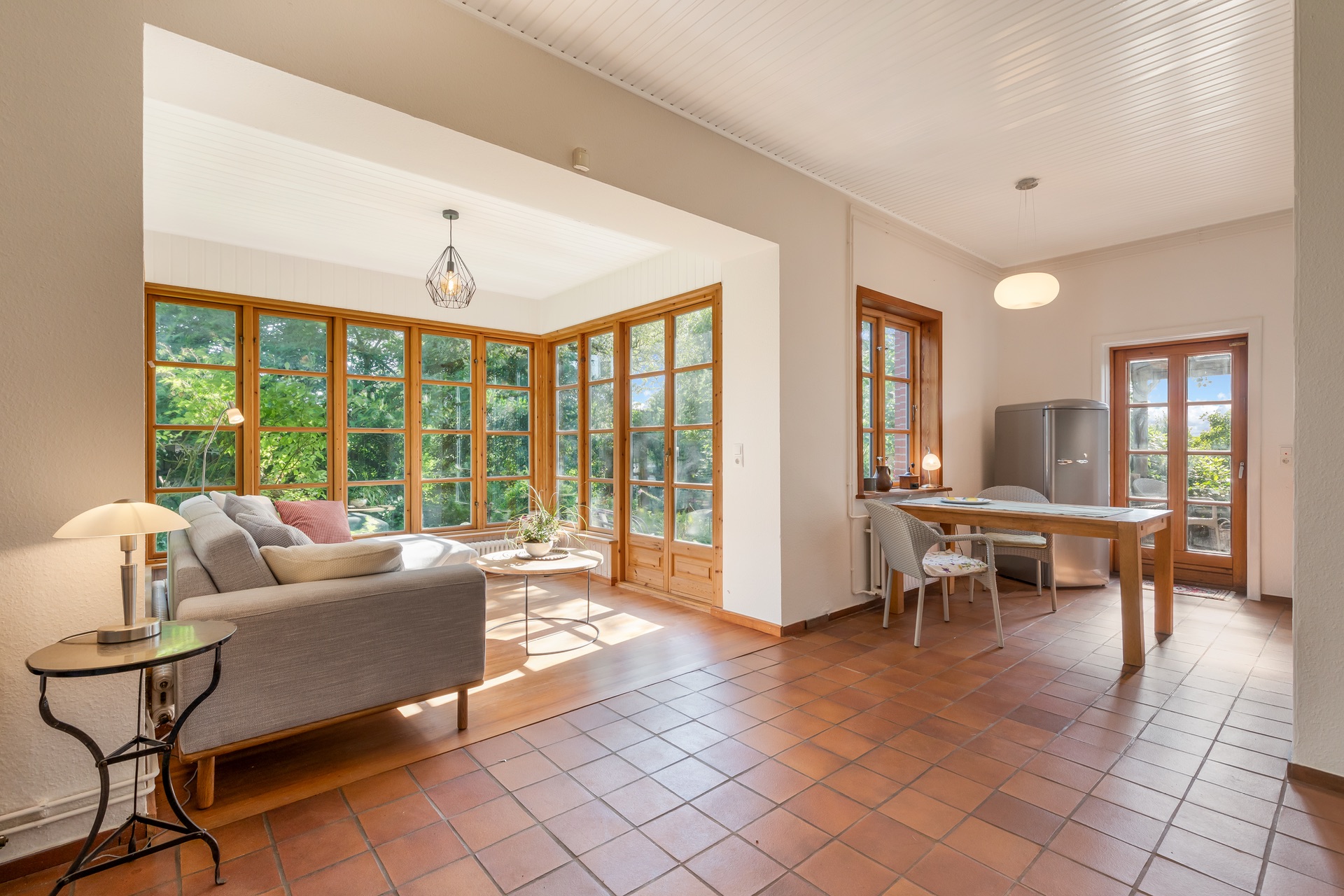 Helles Wohnzimmer mit Sofa, Esstisch und großen Fenstern mit Blick auf den Garten.