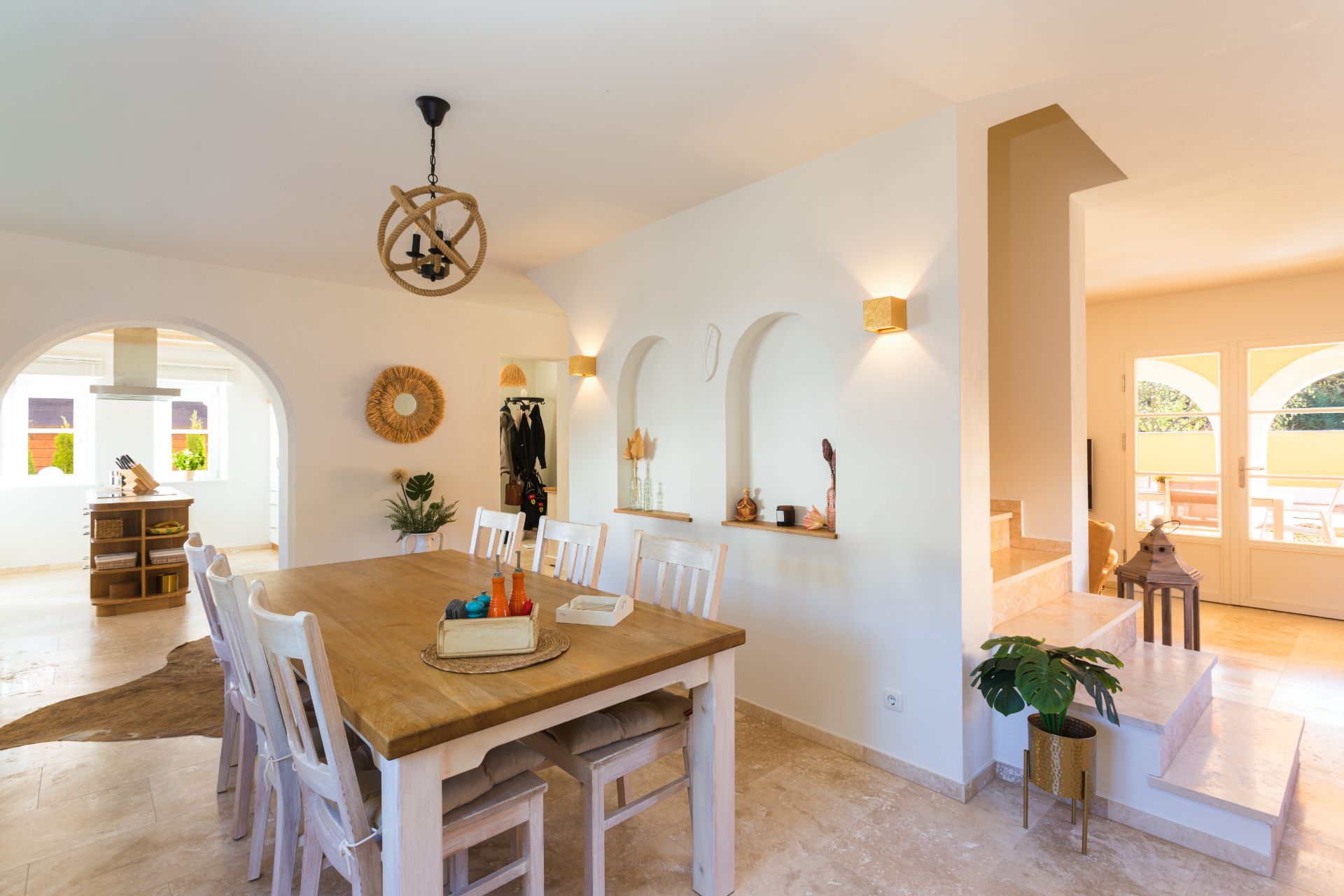 Heller Essbereich mit Holztisch, weißen Stühlen und Dekoration, daneben eine Treppe und große Fenster.