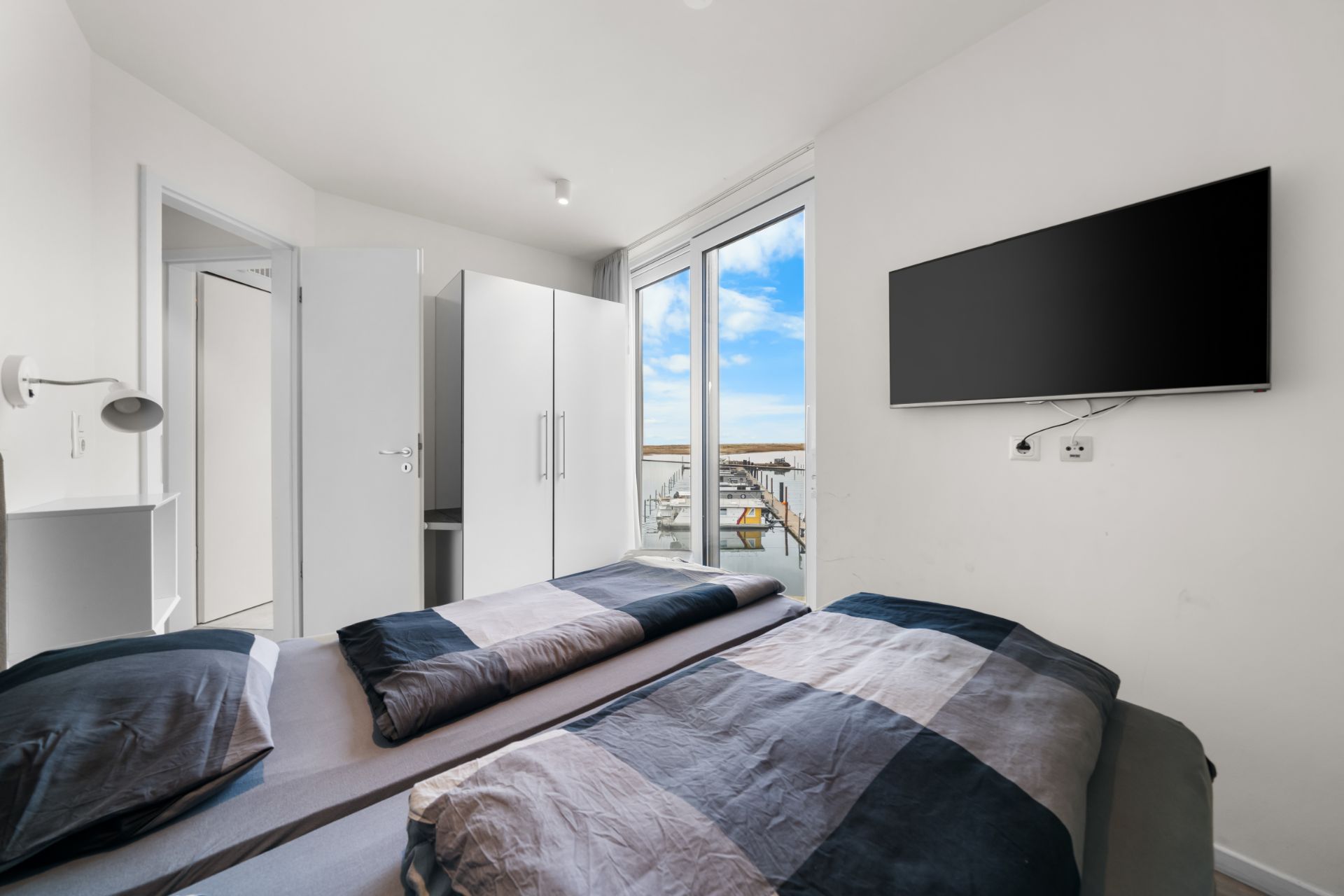 Modernes Schlafzimmer mit Doppelbett, Kleiderschrank, Wand-TV und Fenster mit Blick nach draußen.