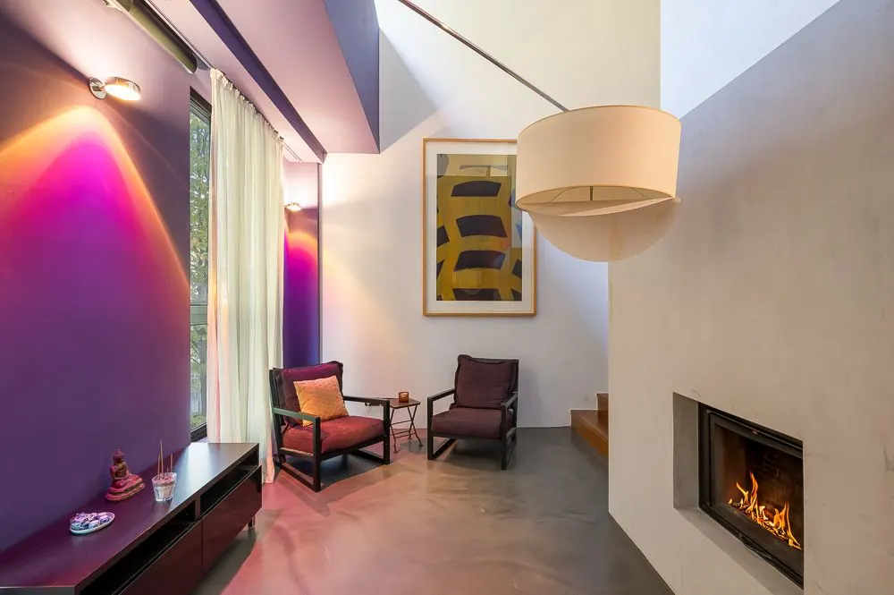 Modernes Wohnzimmer mit lila Wänden, Kamin, zwei Sesseln und abstraktem Bild an der Wand.