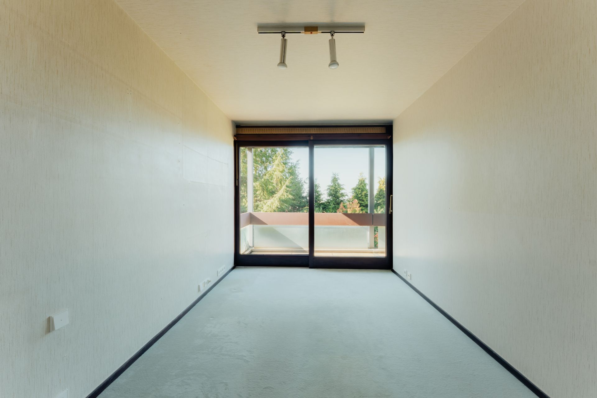Leerer, schmaler Raum mit Teppichboden und großer Fensterfront zur Terrasse.