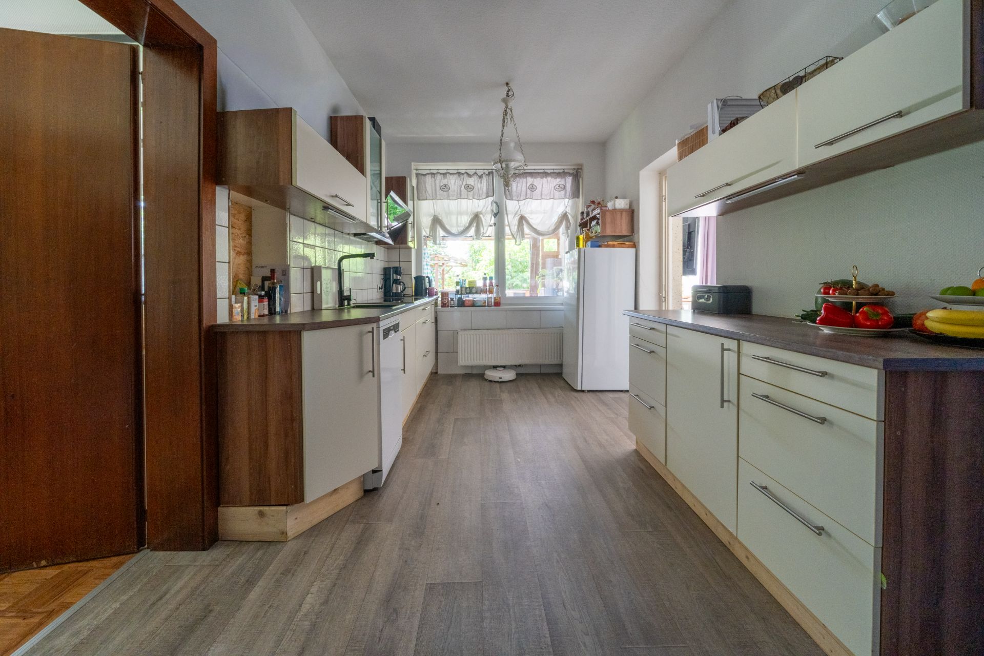 Helle Küche mit weißen Schränken, Holzdetails, großem Fenster und Kühlschrank.