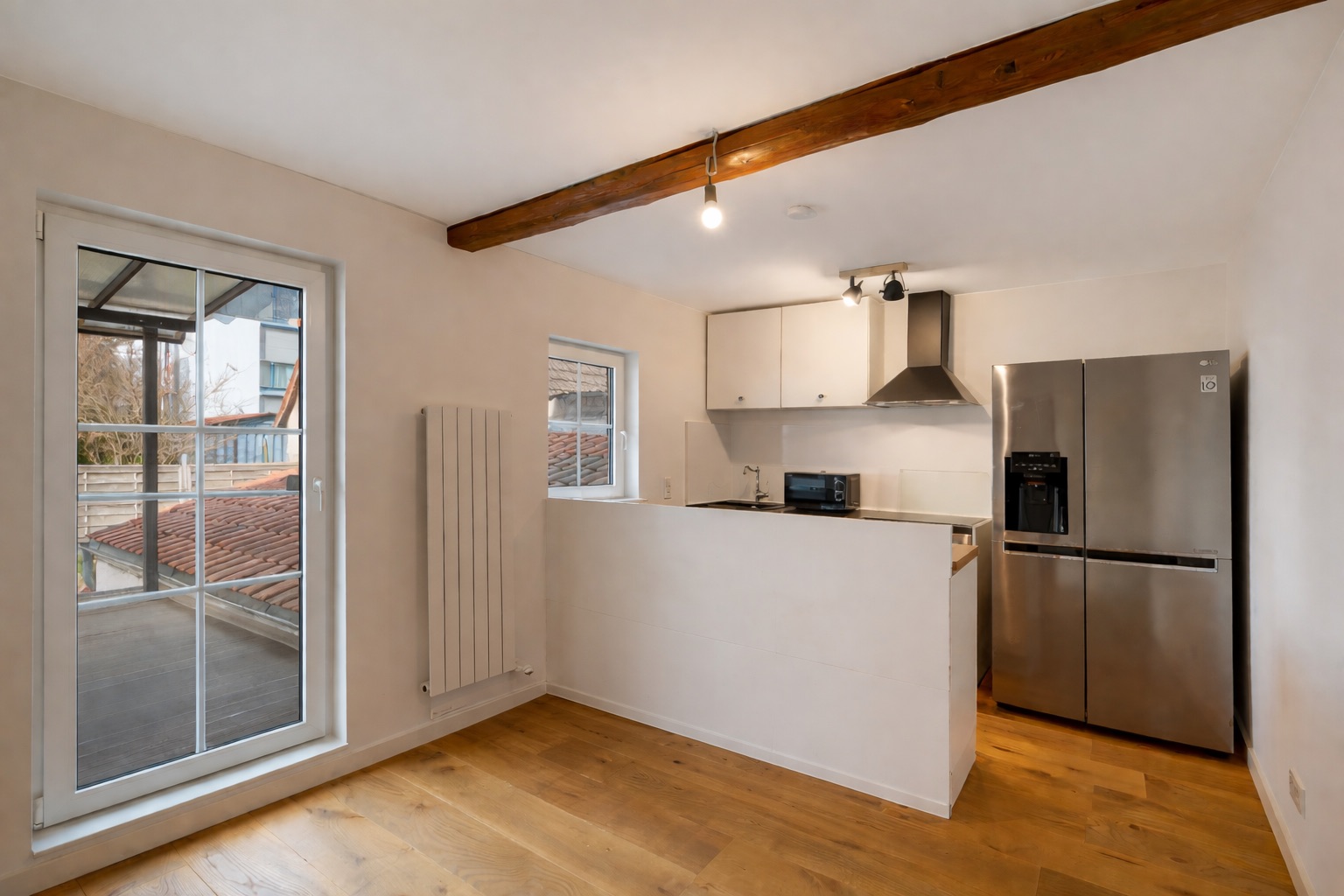 Moderne Küche mit Holzfußboden, großem Fenster, Kühlschrank und weißen Schränken.