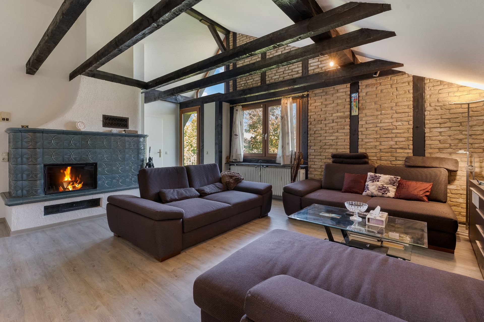 Wohnzimmer mit braunen Sofas, Glas-Couchtisch, Kamin und sichtbaren Holzbalken.