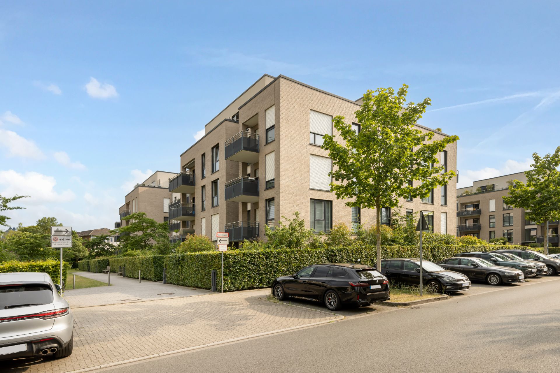 Modernes Mehrfamilienhaus mit Balkonen und parkenden Autos davor an einer Wohnstraße.
