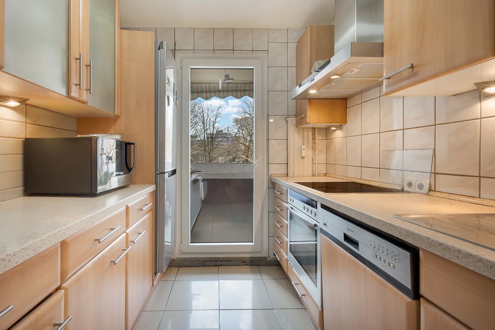 Moderne Küche mit Holzfronten, weißen Fliesen und Zugang zu einem Balkon.