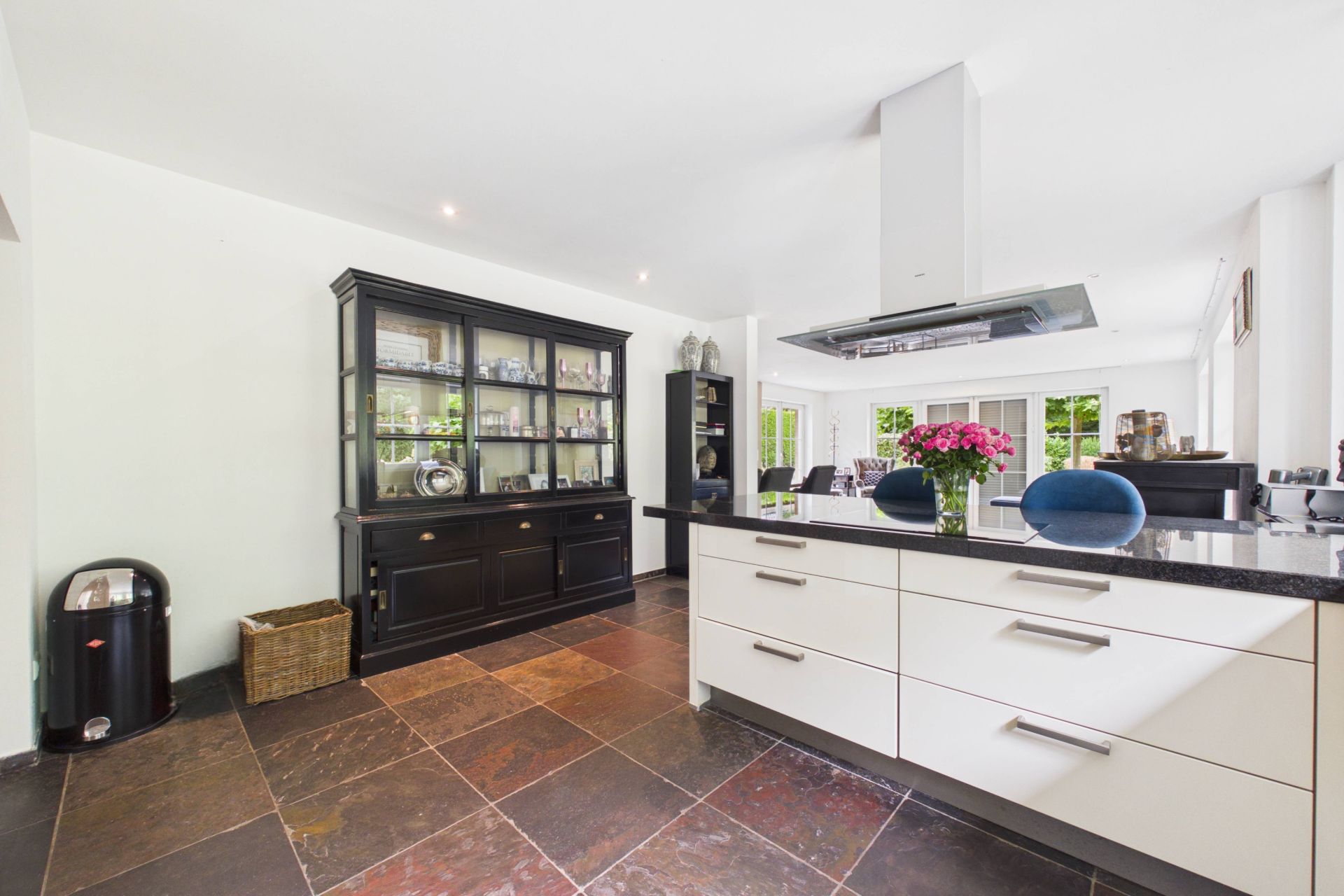 Moderne Küche mit Kücheninsel, schwarzem Schrank, Fliesenboden und Blumenstrauß auf der Theke.