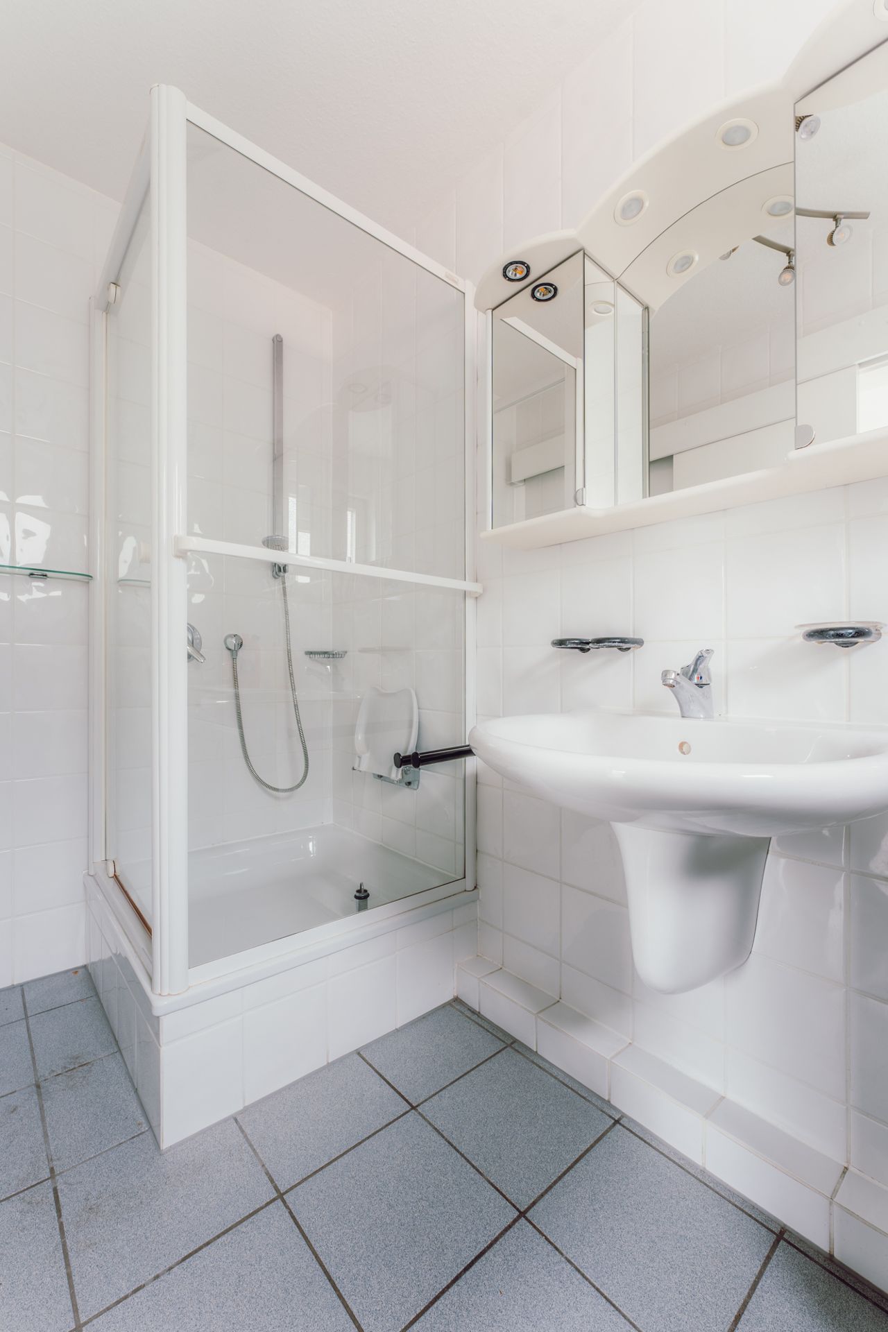 Helles Bad mit Dusche, Waschbecken und Spiegelschrank, weiße Fliesen an Wand und Boden.