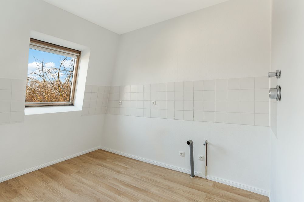 Leerer Raum mit weiß gefliester Wand, Holzboden und einem Fenster.
