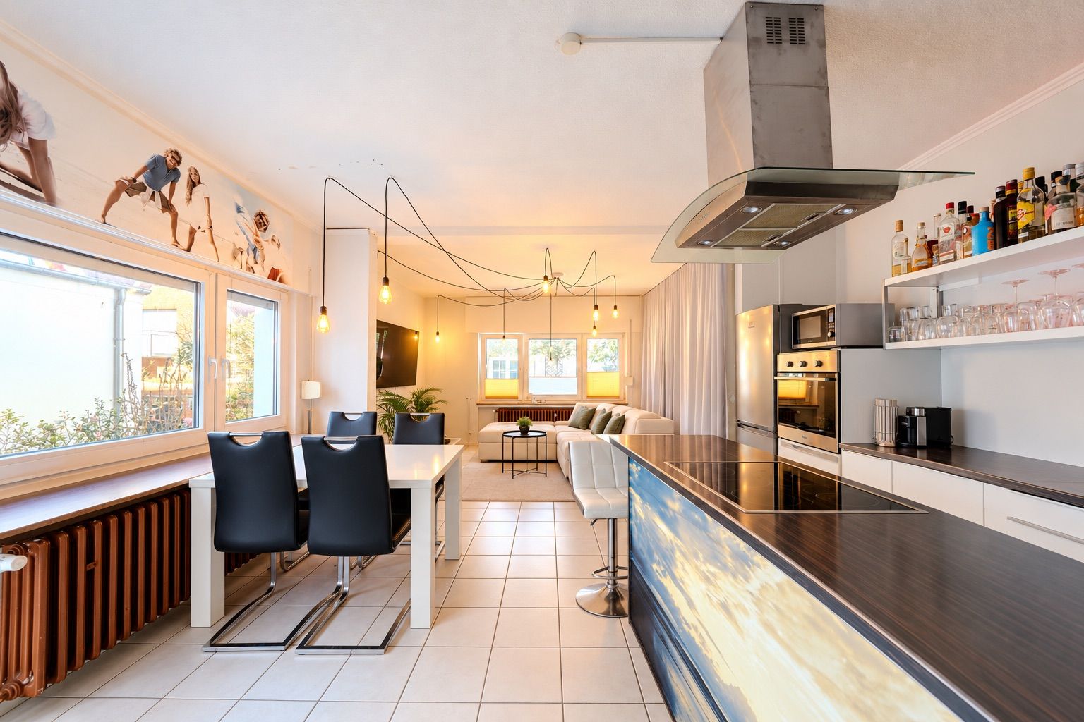 Moderne Wohnküche mit Esstisch, Sofa, großen Fenstern und offener Küchenzeile.