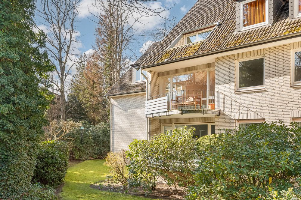 Mehrfamilienhaus mit Garten, Balkon und großen Fenstern, umgeben von Bäumen und Sträuchern.