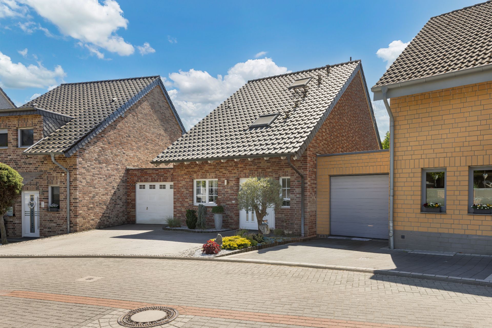 Backsteinhaus mit Satteldach, Garage und kleinem Vorgarten an einer ruhigen Straße.