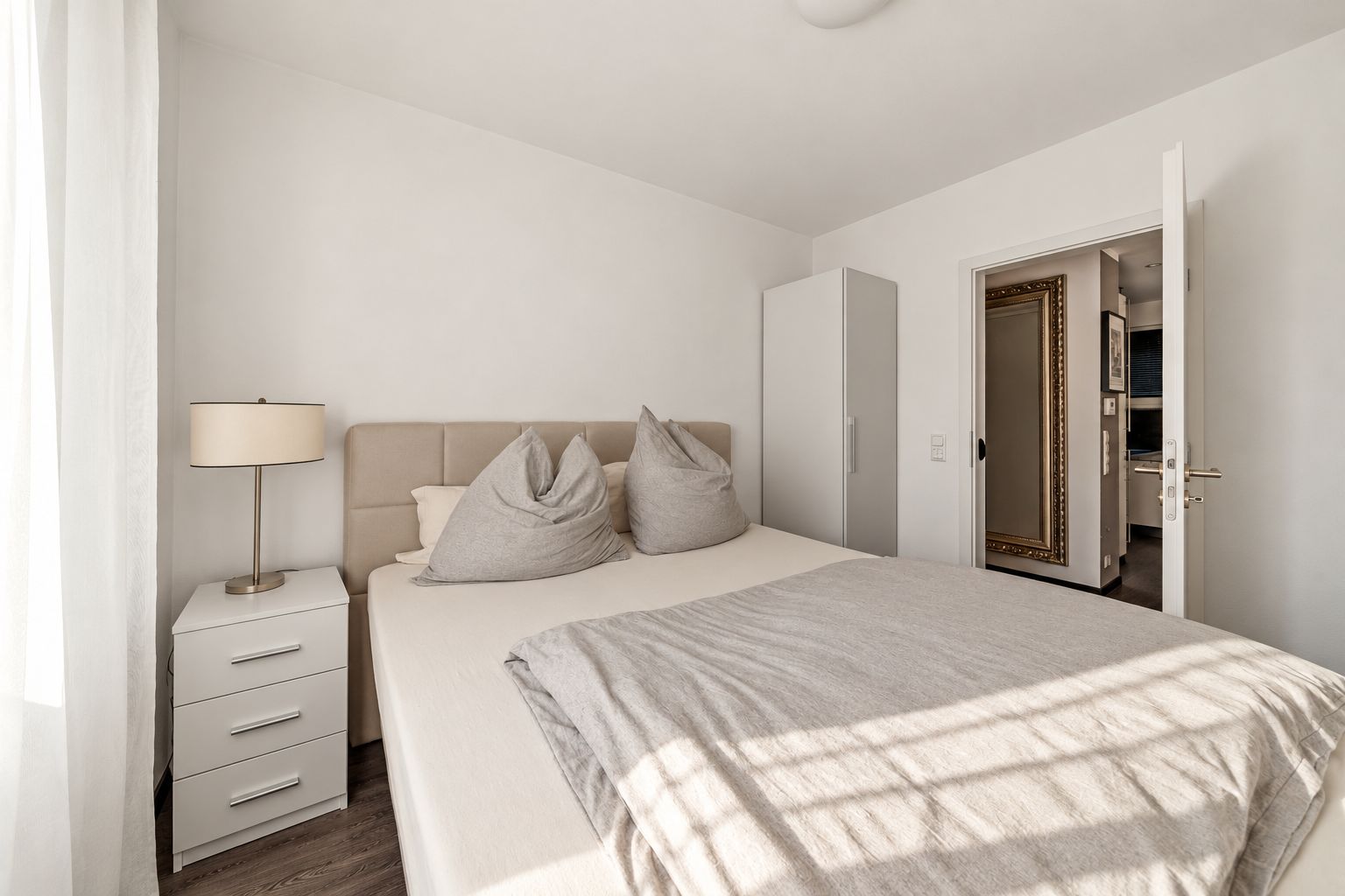 Helles Schlafzimmer mit Doppelbett, Nachttisch, Lampe und Kleiderschrank.