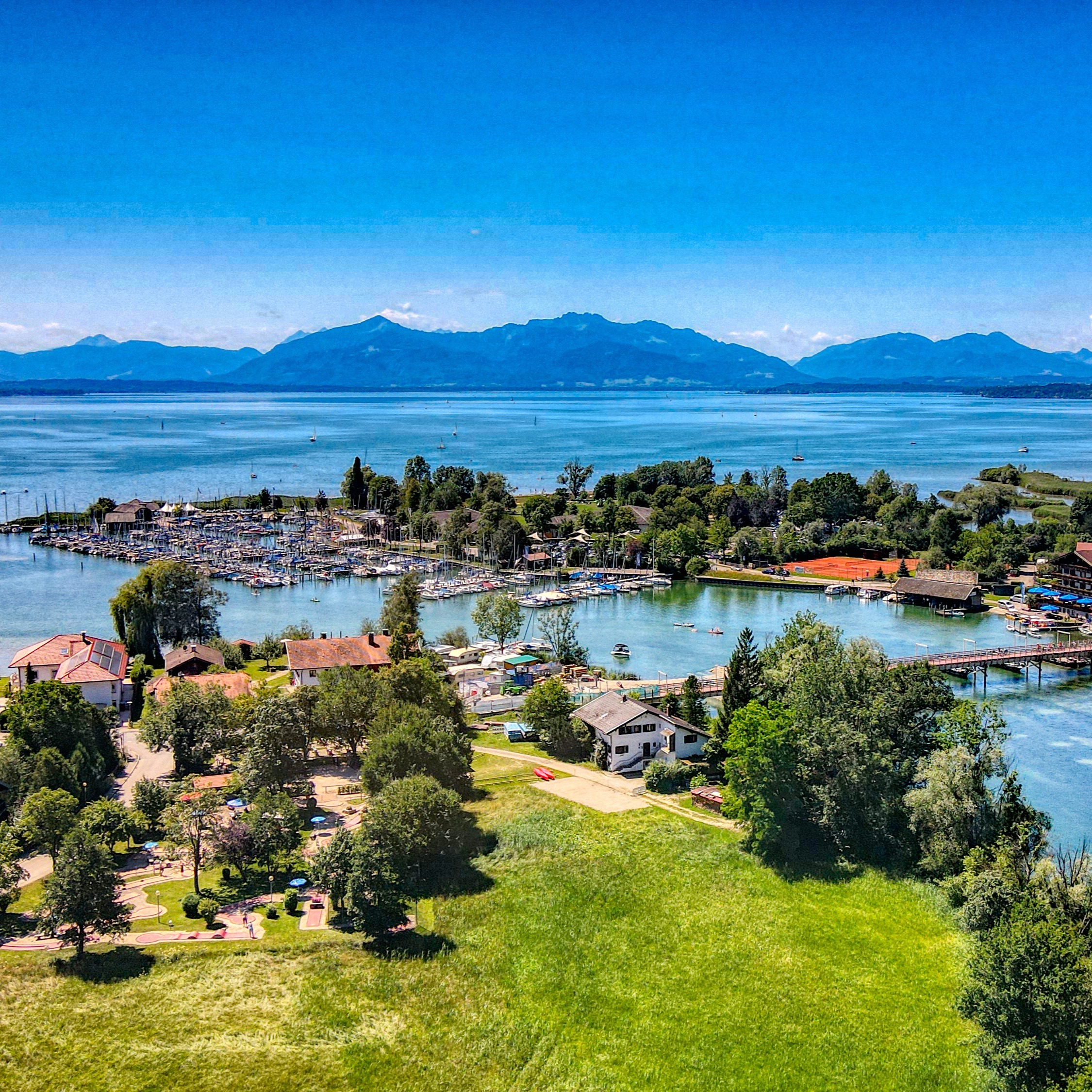 Luftaufnahme eines Wohngebiets am Wasser mit Bäumen, Bootsanlegern und Bergen im Hintergrund.