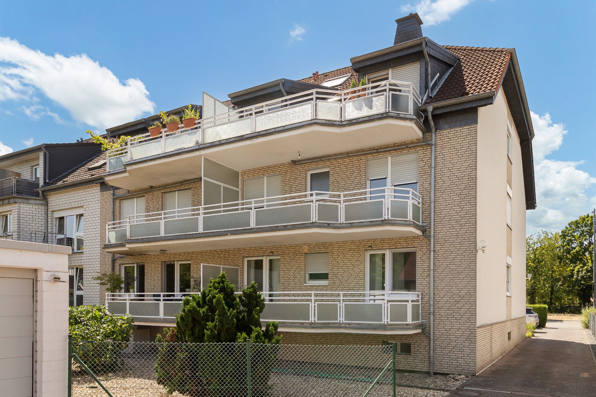 Mehrfamilienhaus mit Balkonen, hellem Klinker und Vorgarten bei sonnigem Wetter.