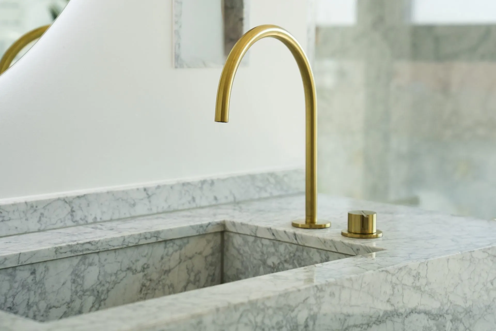 Marmorwaschbecken mit goldfarbenem Wasserhahn auf weißer Arbeitsfläche.
