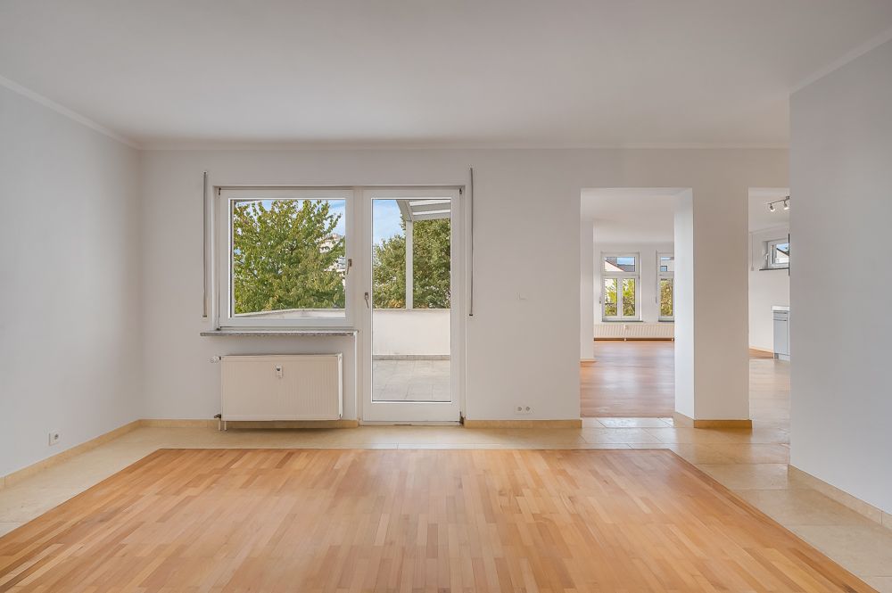 Helles, leeres Wohnzimmer mit Holzboden, großen Fenstern und Zugang zu einer Terrasse.