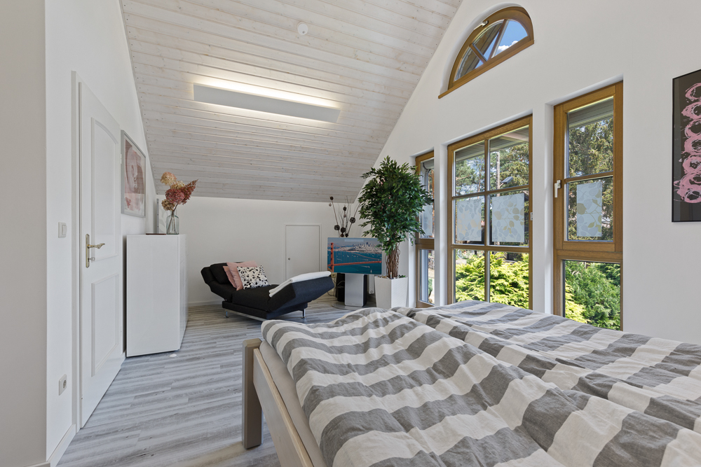 Helles Schlafzimmer mit Doppelbett, großen Fenstern, Sofa und Zimmerpflanzen.