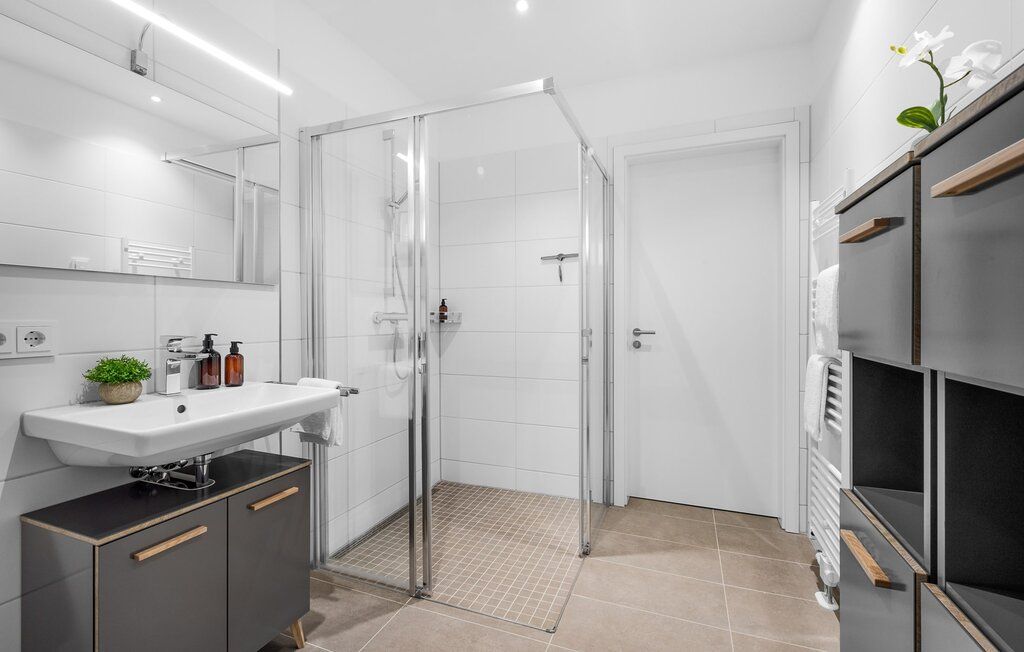 Modernes Badezimmer mit Glasdusche, Waschbecken und hellen Fliesen.