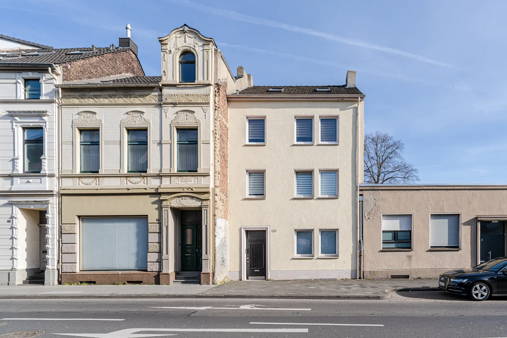 Mehrstöckiges Wohnhaus mit beigen Fassaden, vielen Fenstern und einer schwarzen Haustür an einer Straße.