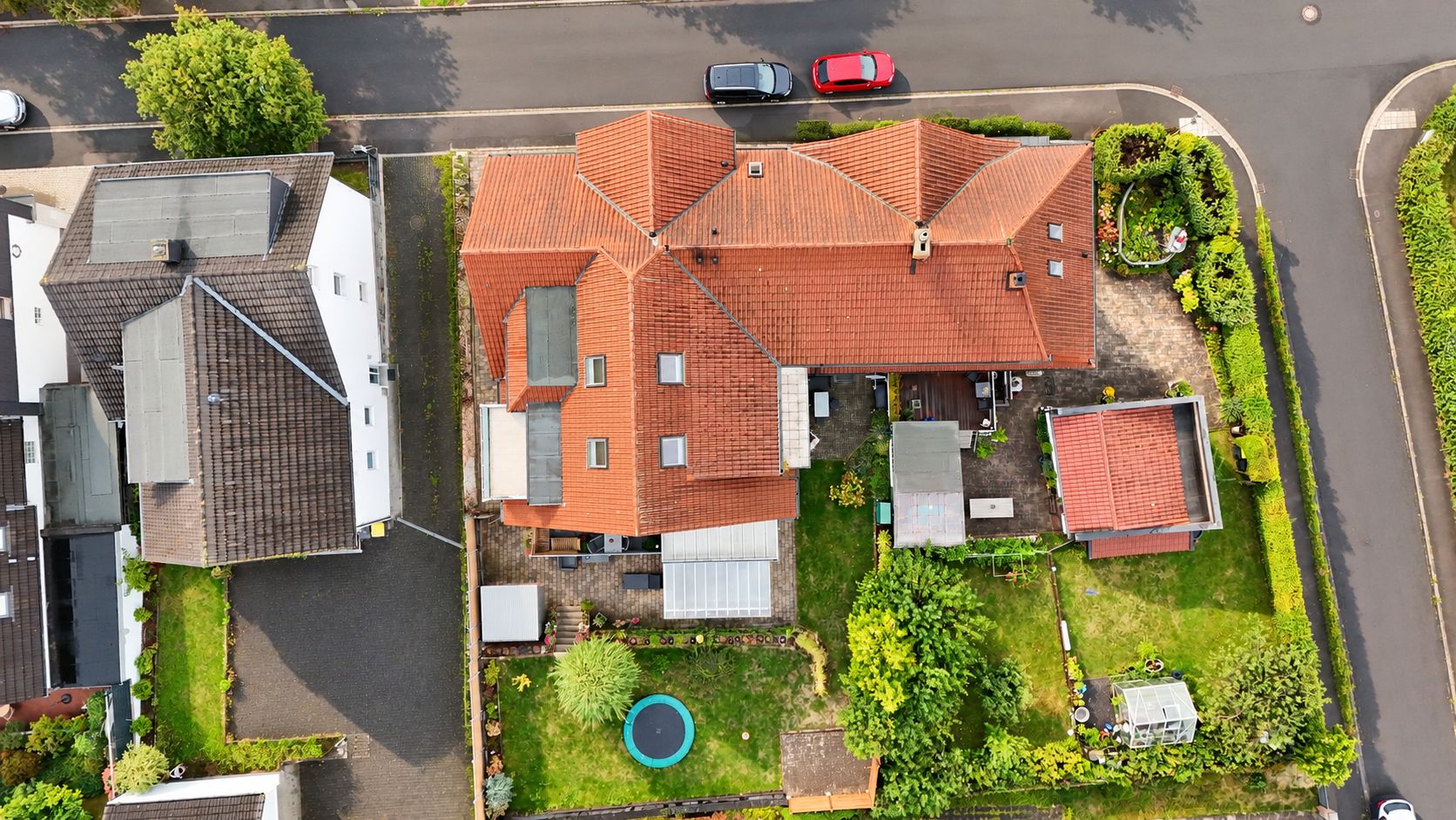 Luftaufnahme eines Hauses mit rotem Dach, Garten, Terrasse und kleinem Nebengebäude.
