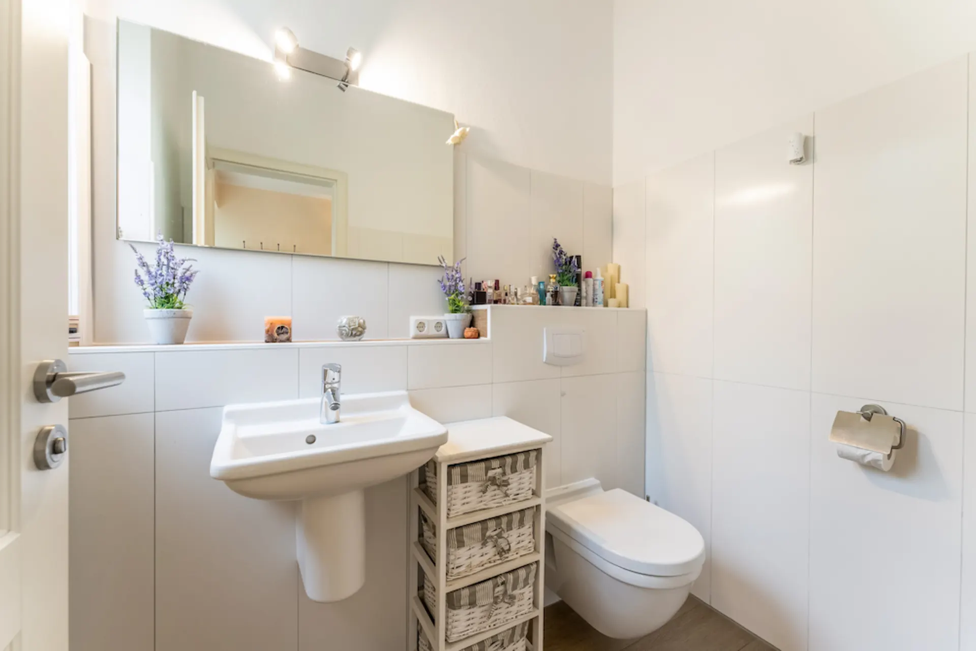 Helles Badezimmer mit großem Spiegel, Waschbecken, WC und Dekoration wie Lavendel und Kerzen.