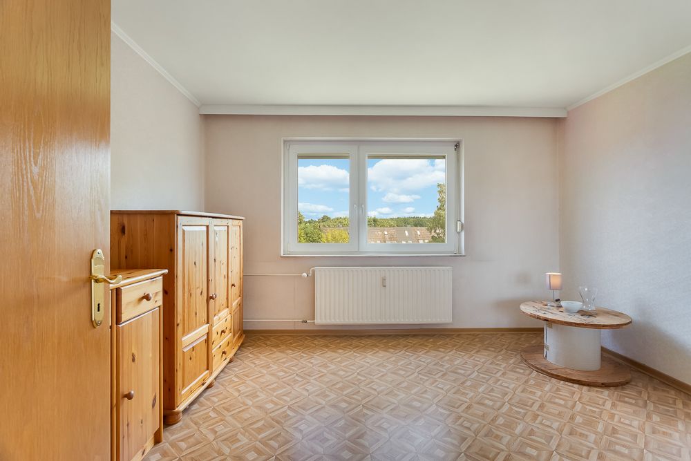 Helles Zimmer mit Holzschrank, rundem Tisch und großem Fenster mit Ausblick.