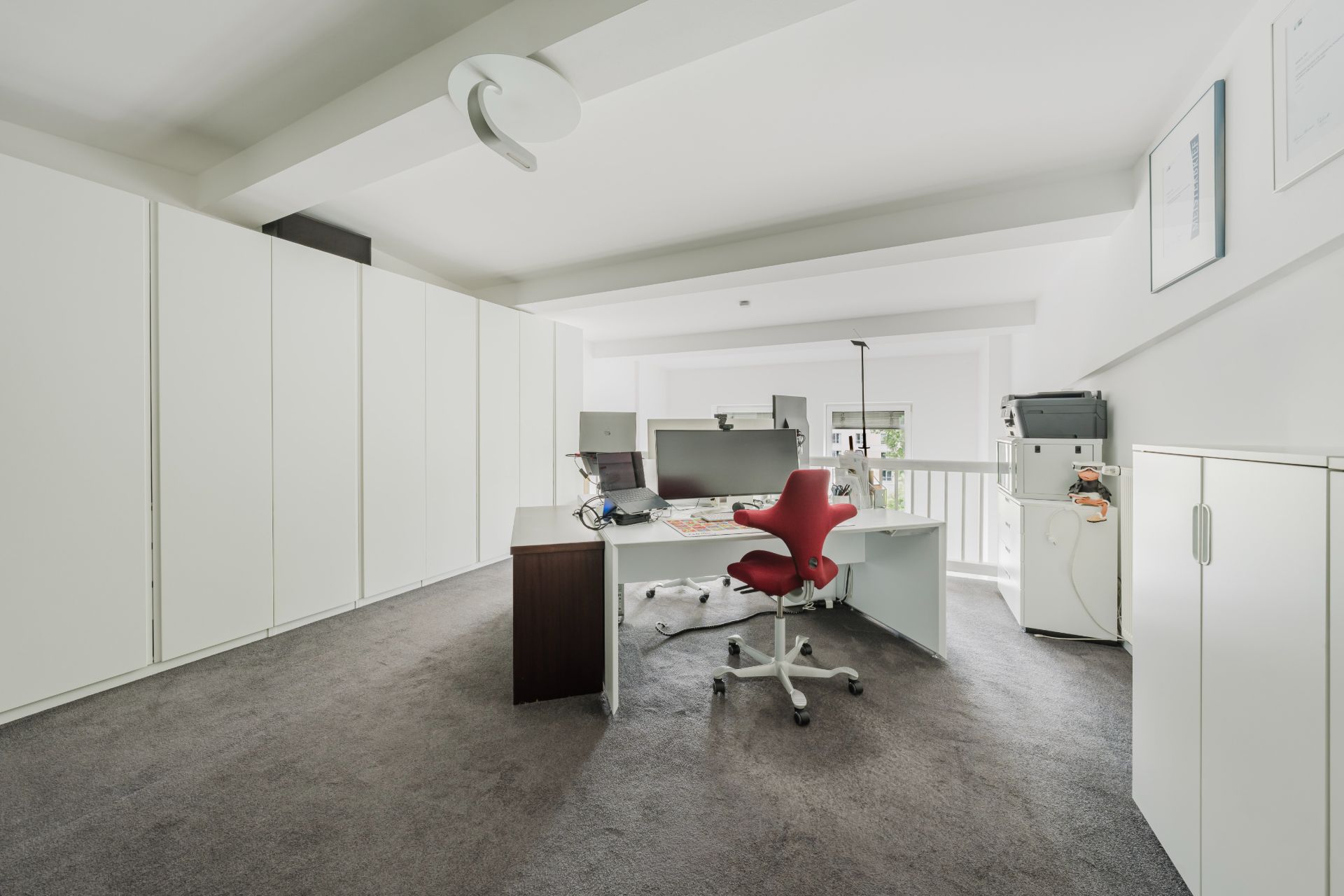 Modernes Arbeitszimmer mit großem Schreibtisch, rotem Stuhl und weißen Schränken.